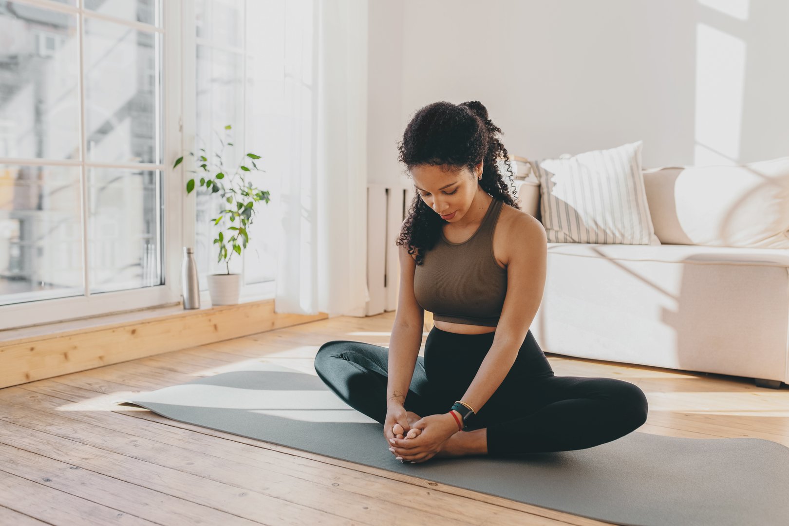 Active african american pregnant woman practicing yoga, sitting in butterfly or konasana pose, stretching muscles on mat, doing prenatal exercises for healthy pregnancy and prepare body for childbirth
