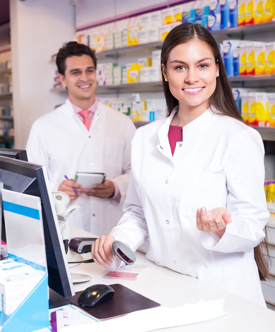 Smiling young professional pharmacist at reception of drugstore ready to help