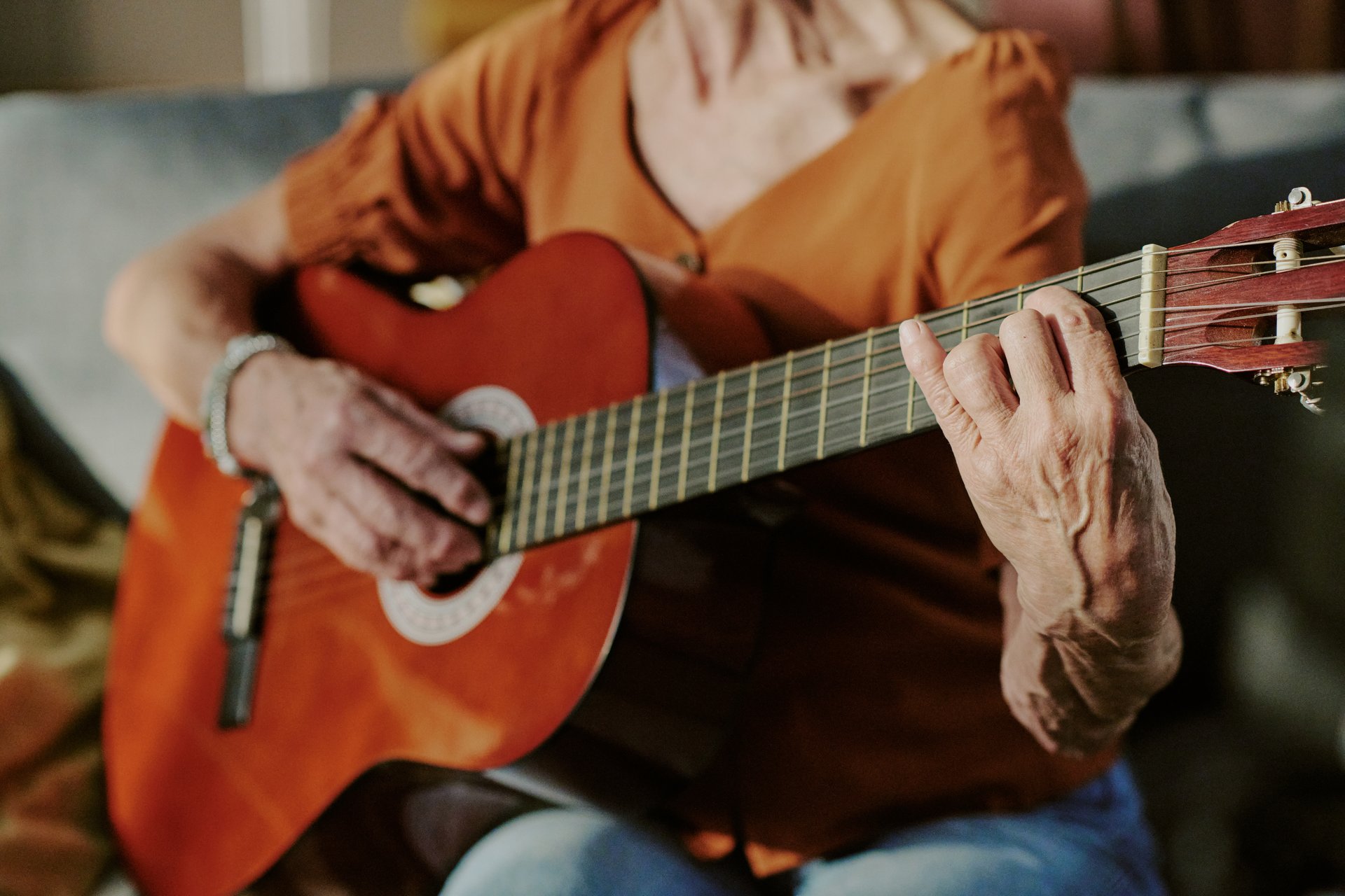 Senior person playing acoustic guitar while sitting comfortably