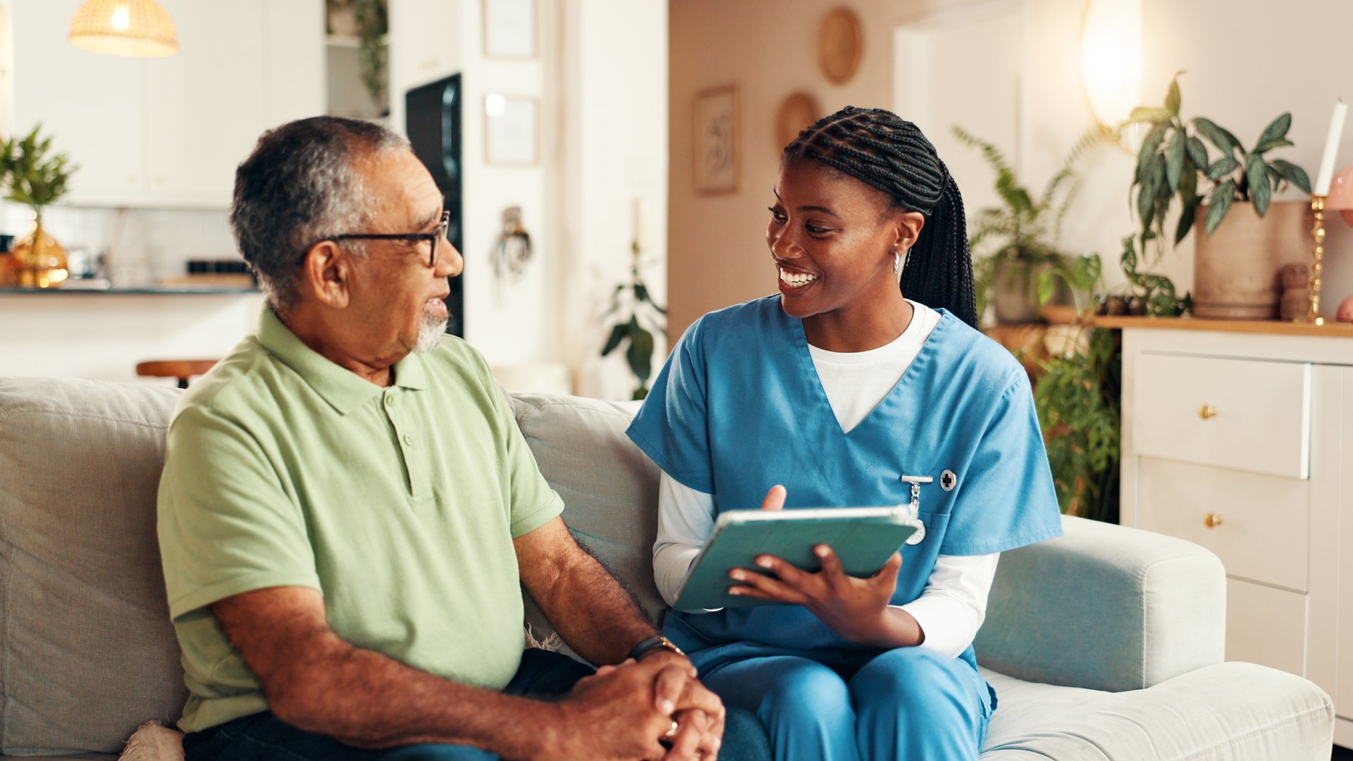 Nurse, senior man and tablet on sofa with smile for wellness, medical update and report in lounge. Woman, caregiver and elderly patient on couch with digital touchscreen, app and healthcare results