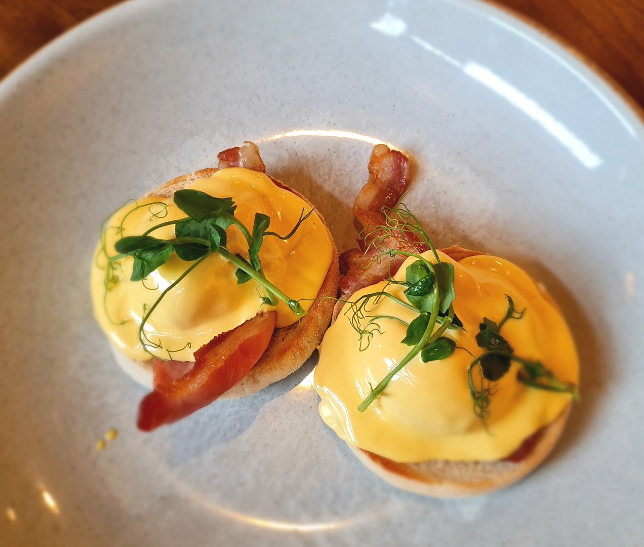 View from above of plate of eggs benedict breakfast with poached eggs smoked bacon and hollandaise sauce on blue plate