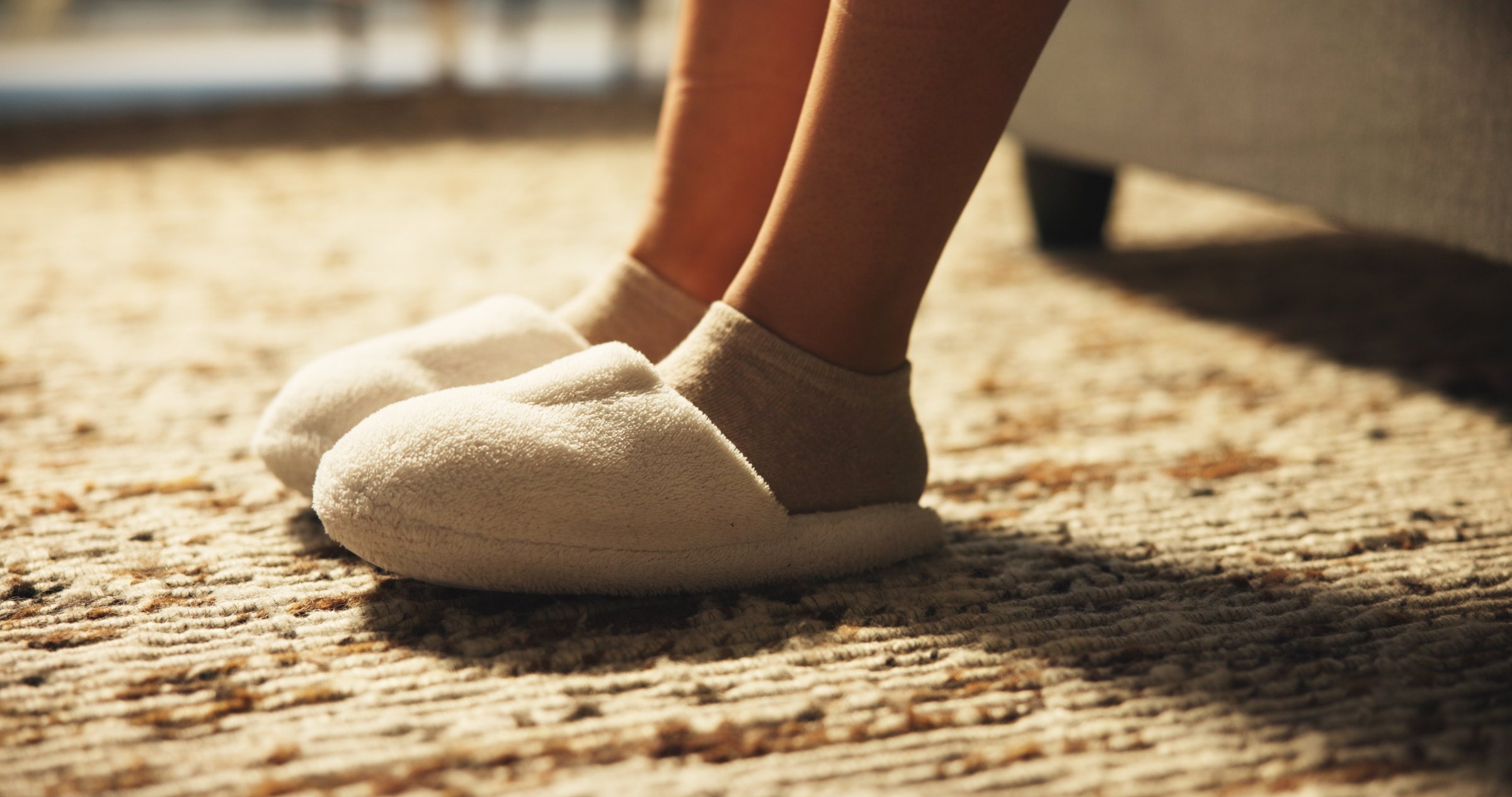 Person, legs and slippers in bedroom at house from sleeping, wake up and morning routine. Closeup, feet and woman with shoes, comfortable footwear and getting ready to start day, bed rest and cozy