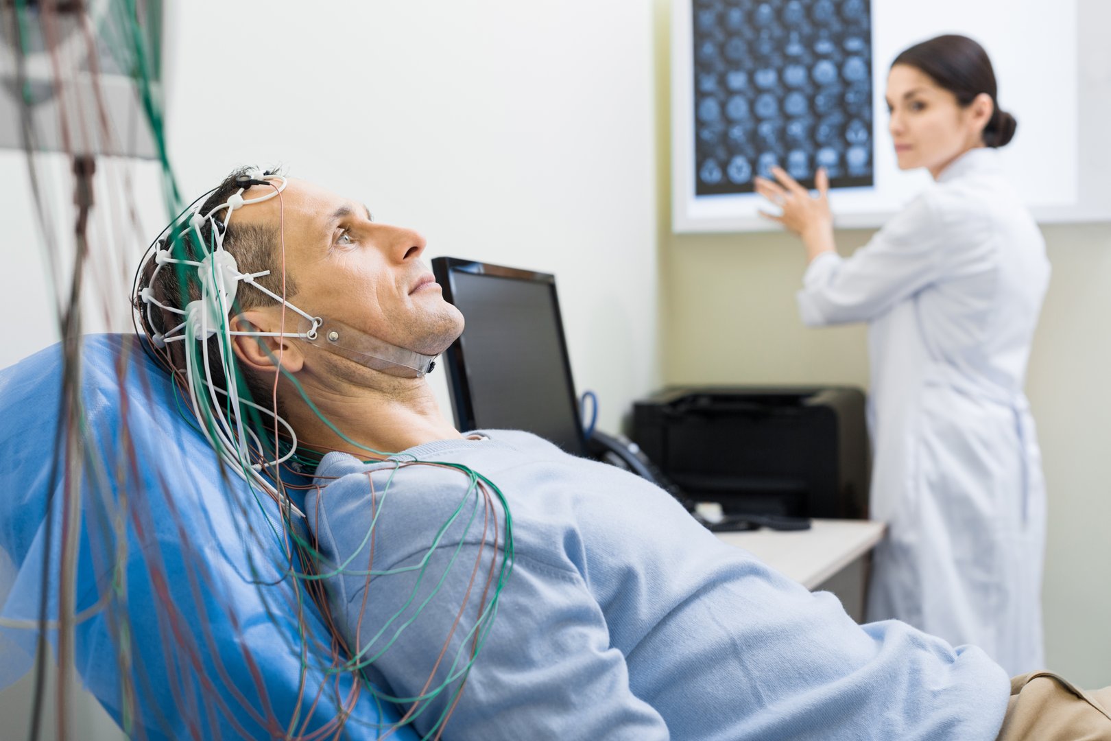 Best healthcare service. The focus being on a handsome middle-aged man undergoing electroencephalography while his doctor studying his CT scan results