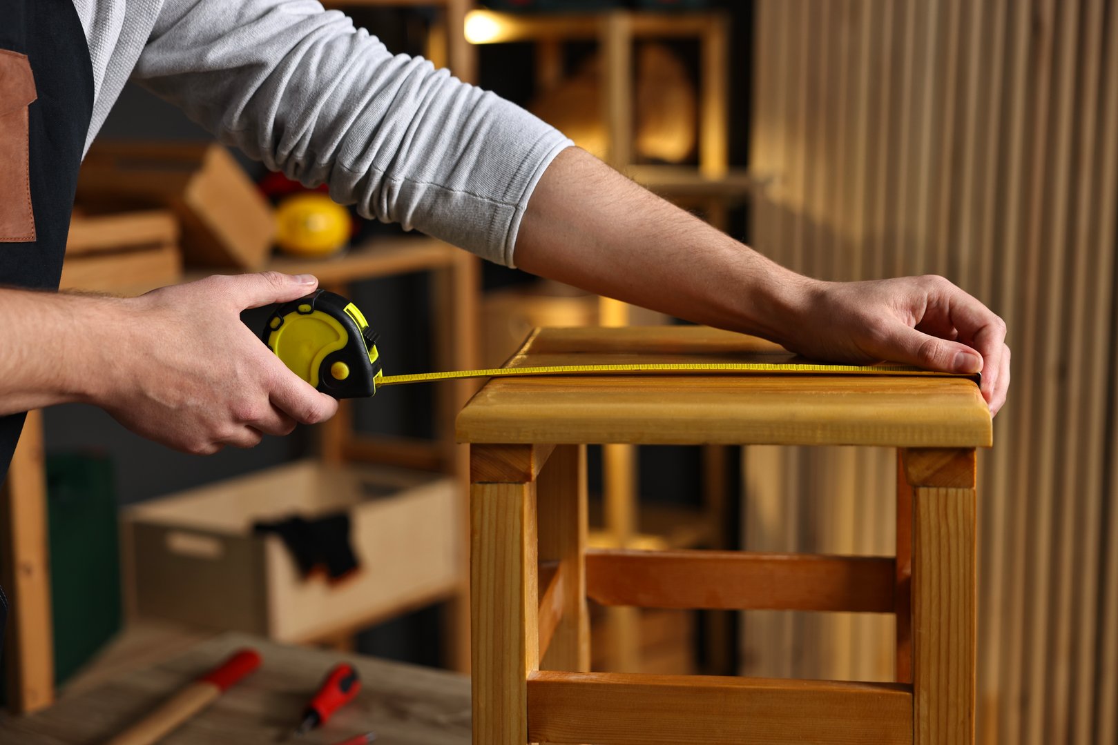 Repairman measuring wooden stool in workshop, closeup
