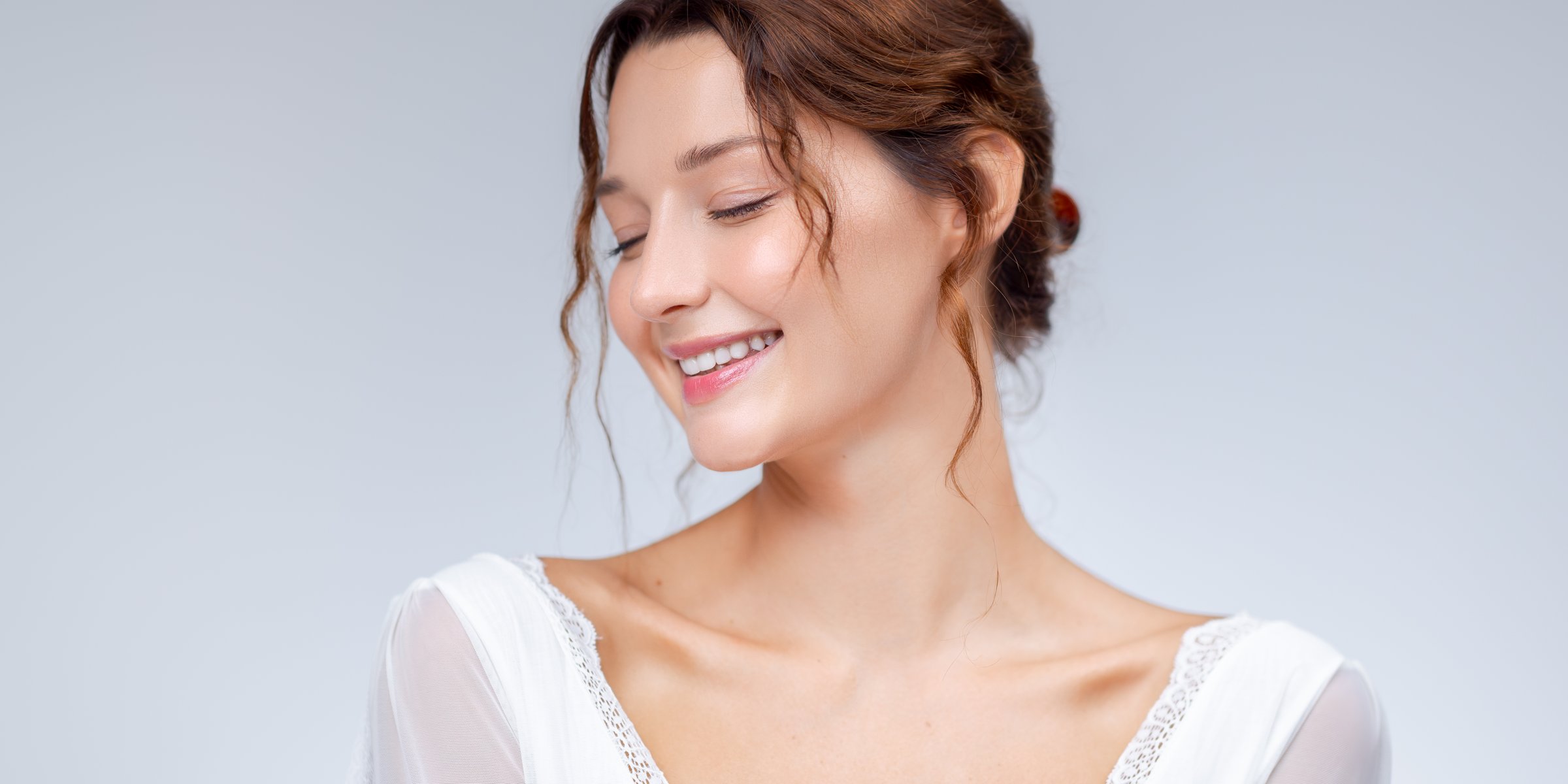 Charming woman in a white lace-trimmed dress smiles gently while looking down. Perfect for bridal beauty, skincare branding, minimalist fashion, and wellness-focused visuals.