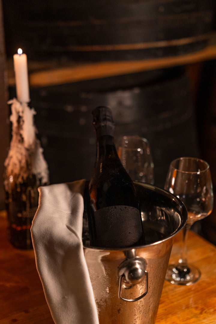 Chilled Lambrusco wine in an ice bucket with a cloth napkin on a rustic table, candlelight, and barrels in a dimly lit background.