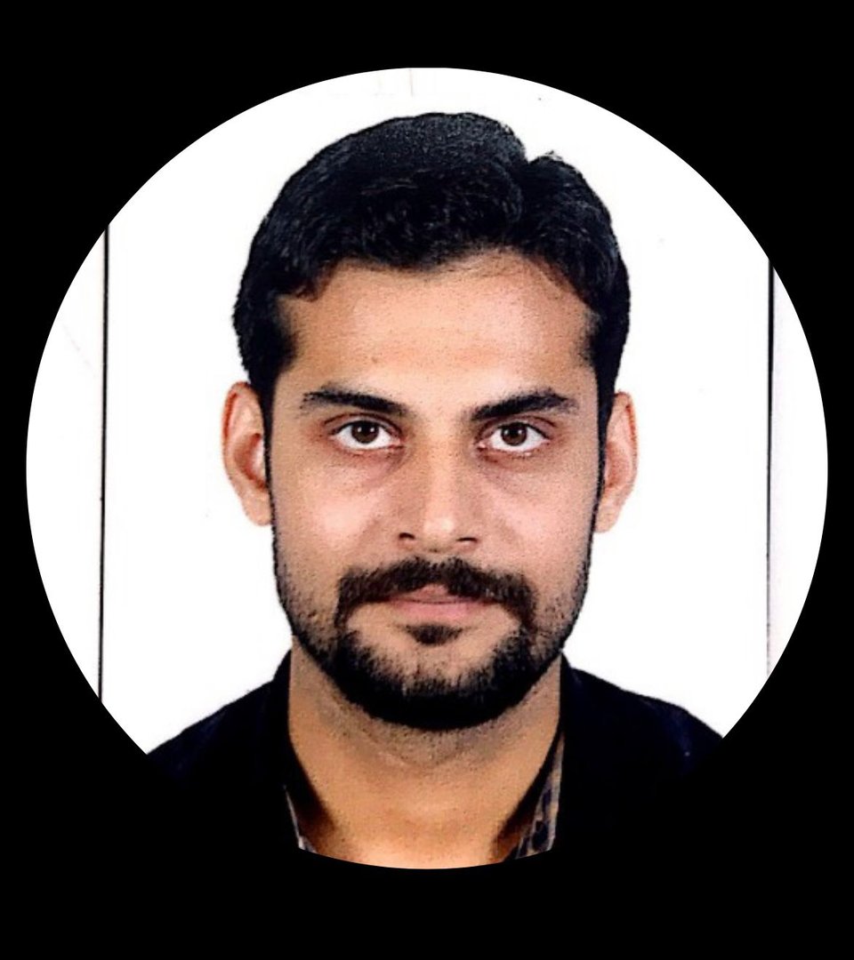 A bearded man with short hair against a white background, wearing a dark shirt and jacket, looking directly at the camera.