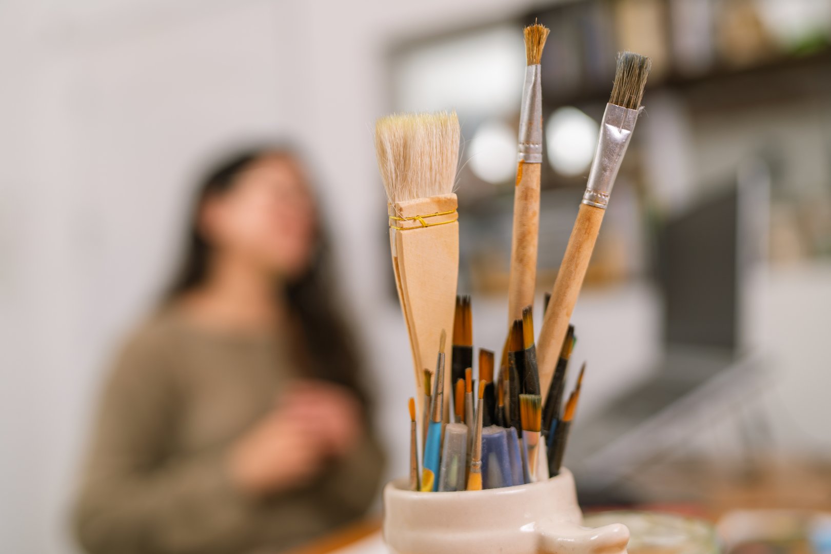 Paintbrushes are arranged in a jar on a desk in a home art studio