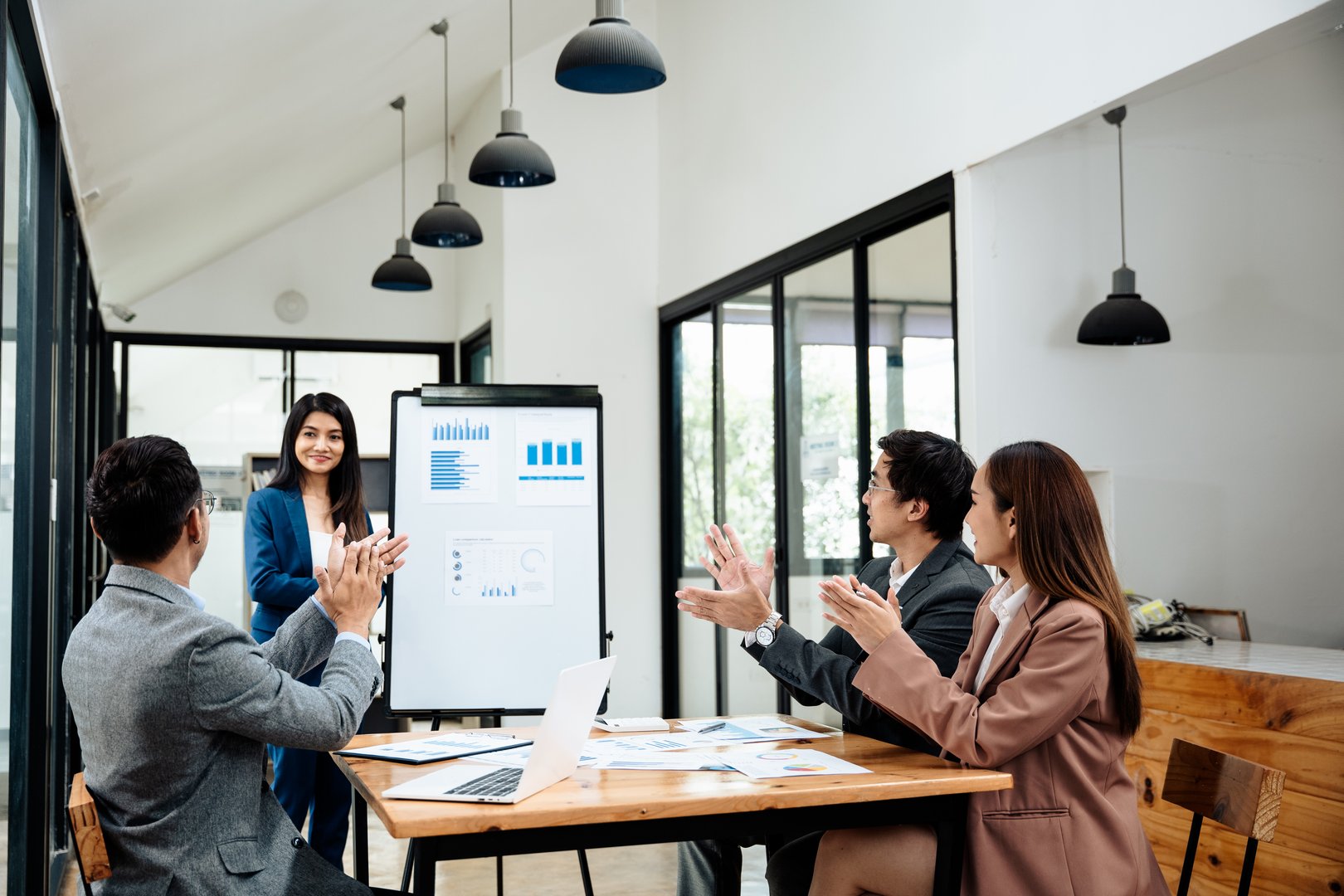 Group of teamwork businesspeople are clapping hands to success and archive on business financial and marketing after working on laptop and paperwork sit on sofa in commonual room