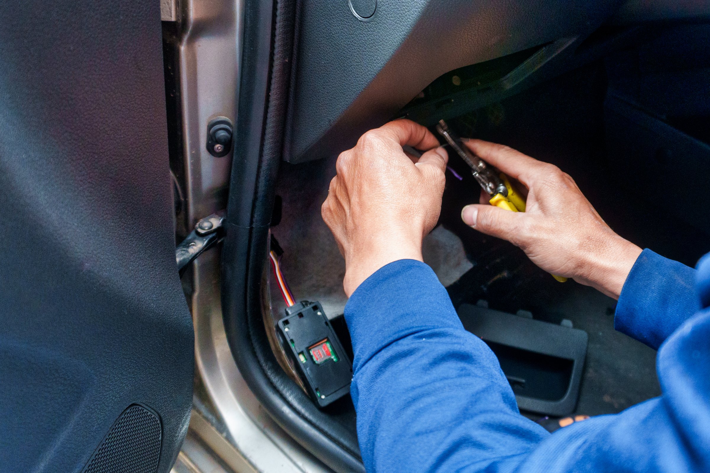 Close-up of a man installing an electronic satellite positioning device in a car. The man is cutting a cable with pliers