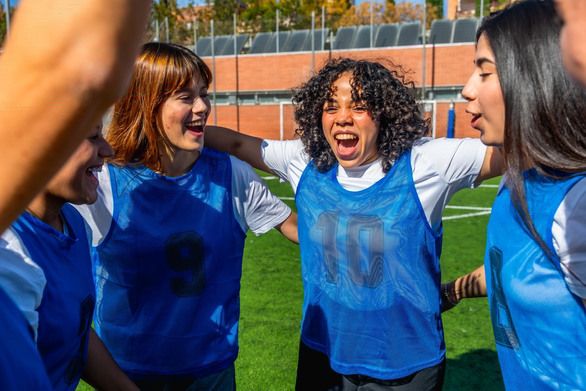 Young diverse women soccer players embrace and cheer on a sunny field, celebrating victory with laughter, teamwork and joyful camaraderie after a successful match