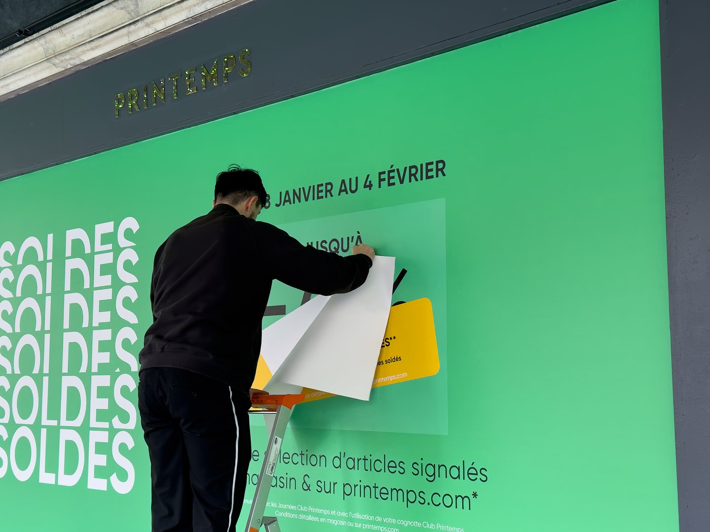 Paris,France-29.01.2025 A worker climbs a ladder to install bright signage advertising winter sales during January and February at a popular shopping location.