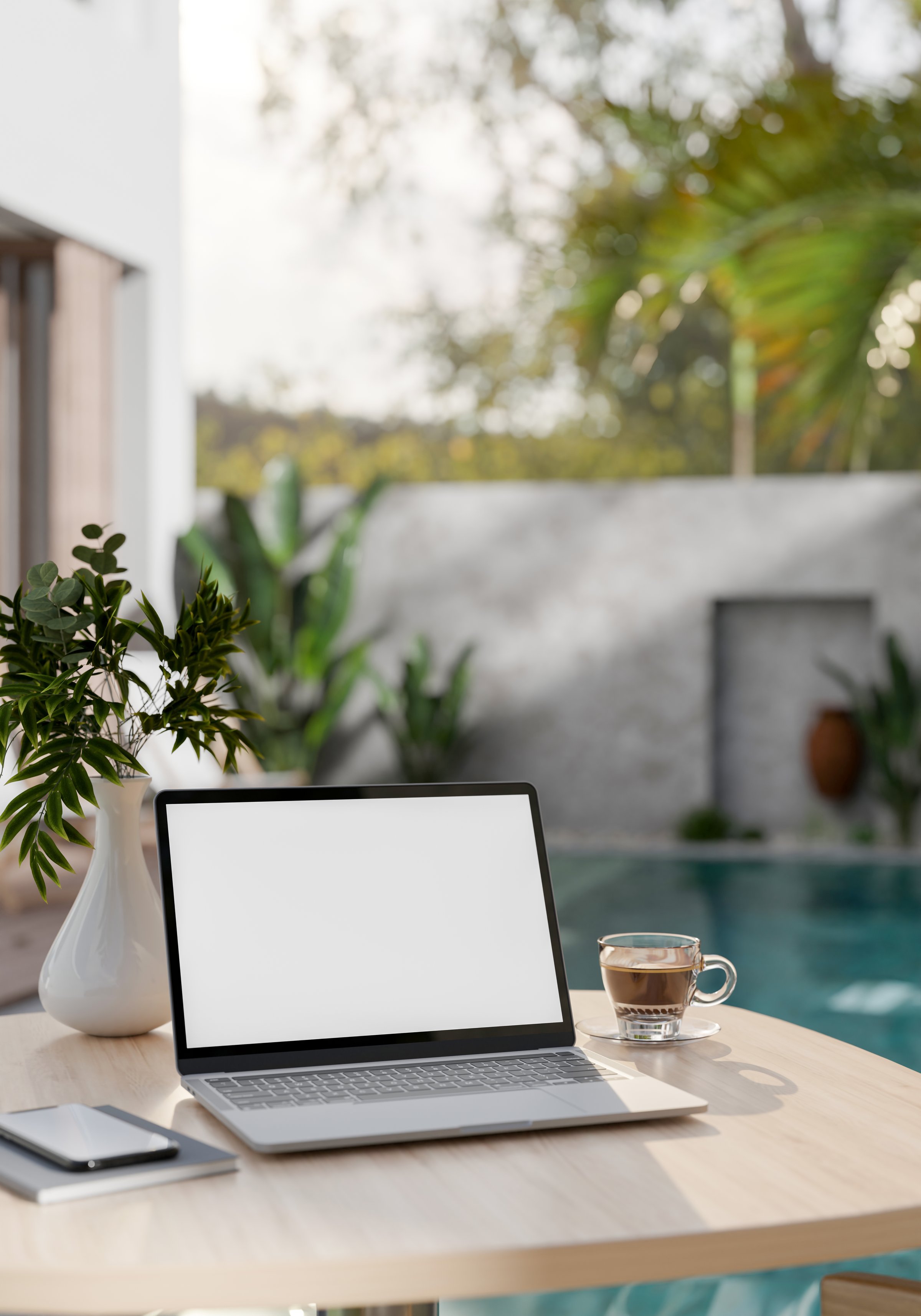 A digital tablet and phone placed next to a coffee cup on wooden table beside the empty swimming pool.