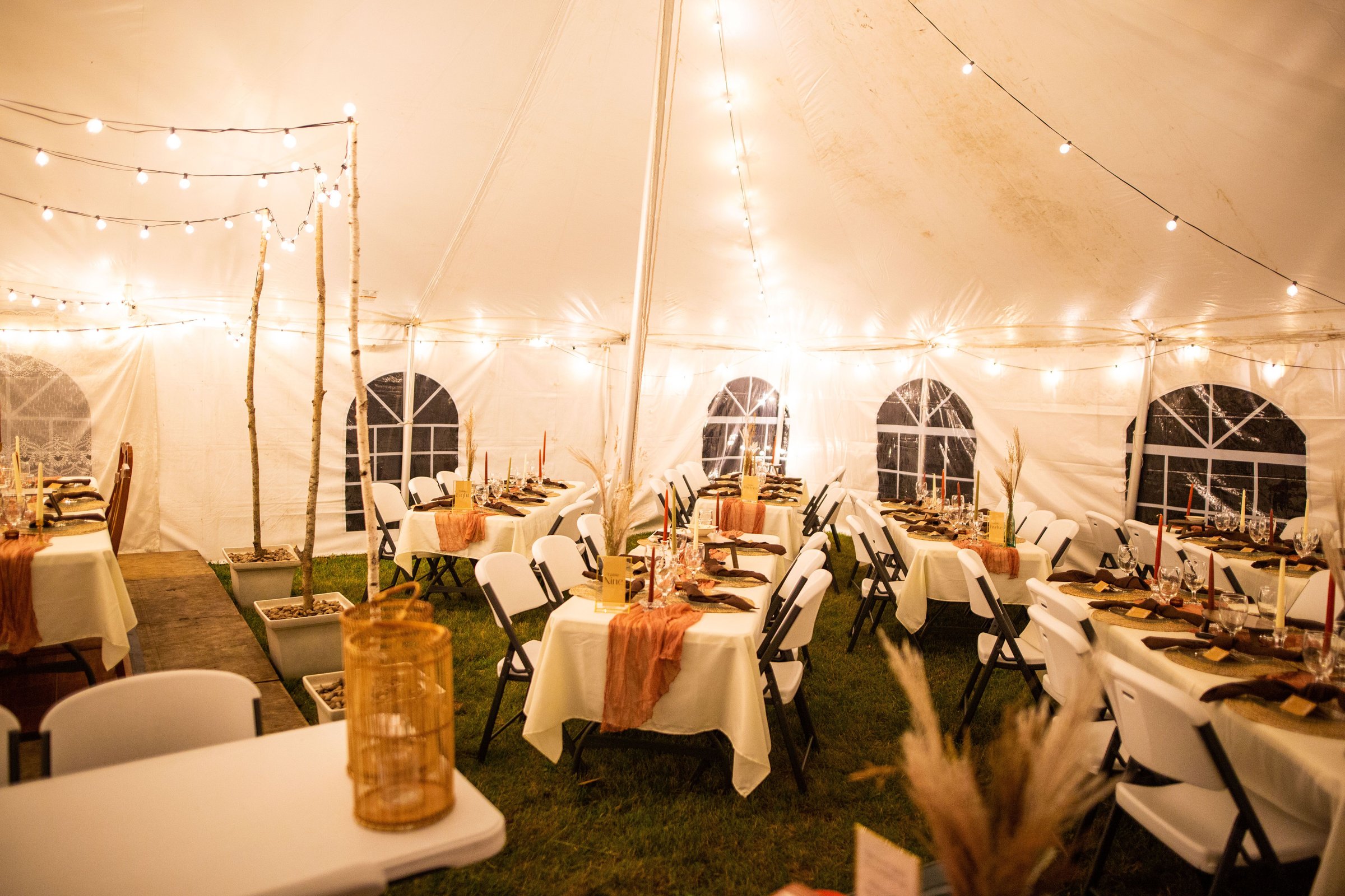 A wedding venue tent with dinner equipment on tables and string lights