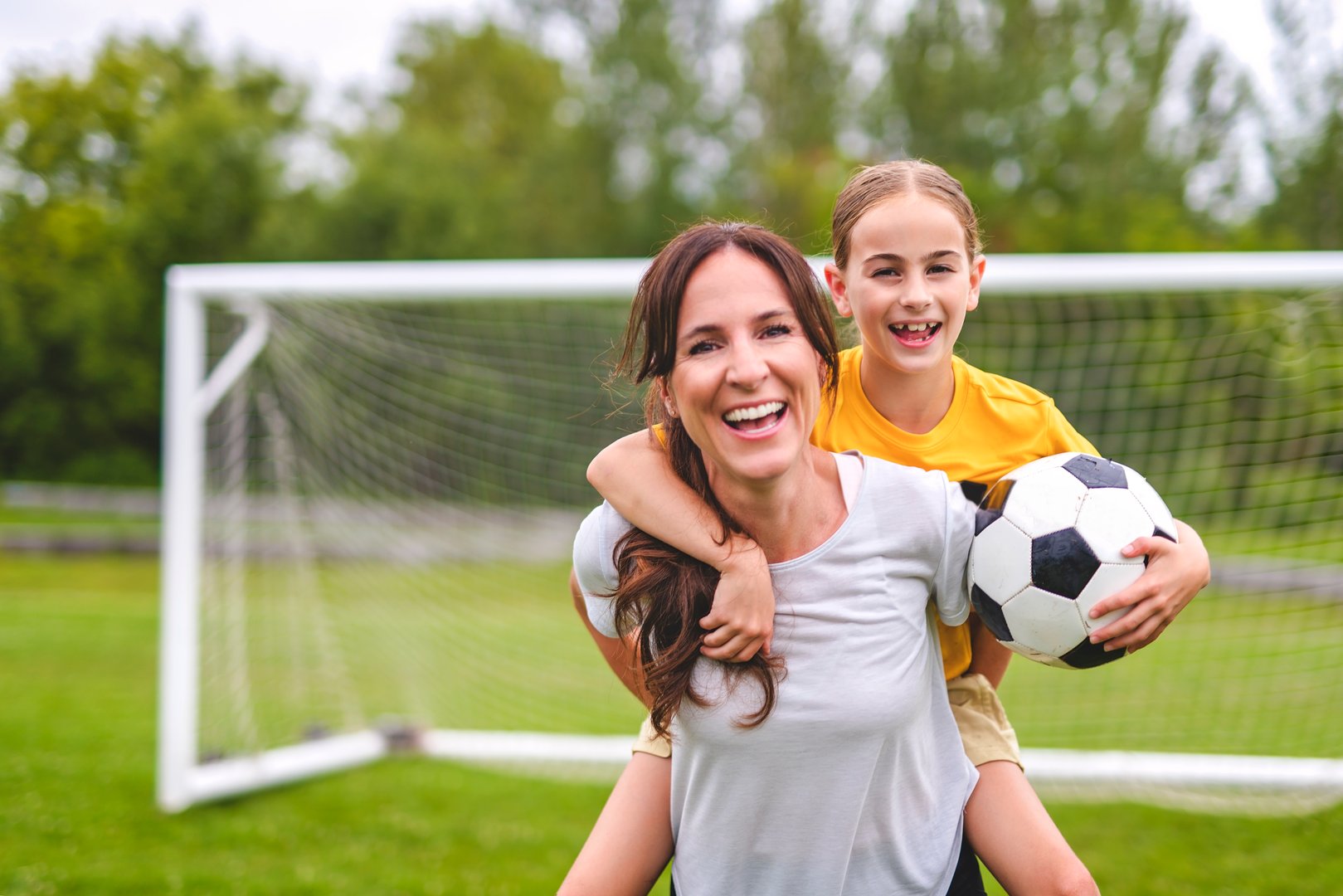 A happy mother playing football outdoor on a summer day with her daughter
