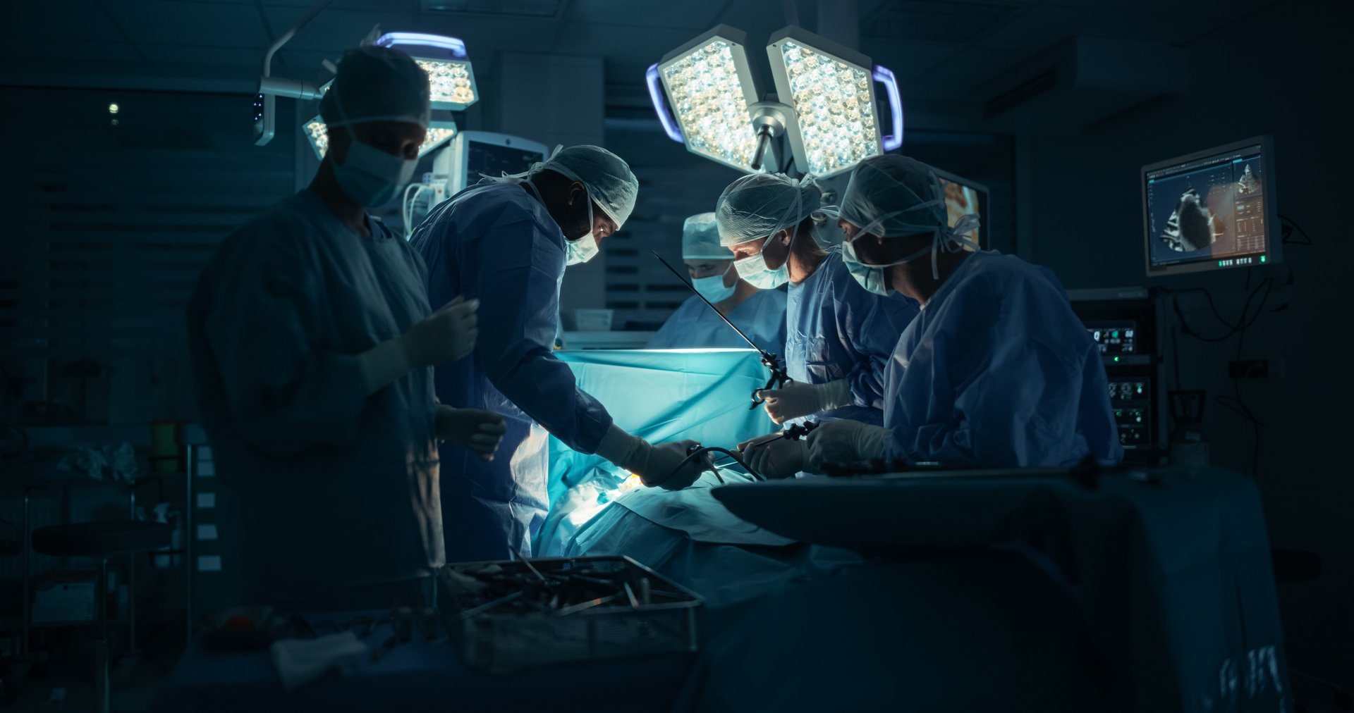 Diverse Surgical Team Working in a Darkened Operating Room Surrounded by Advanced Medical Equipment. Doctors Performing a Complex Surgery with the Help of Laparoscopic Equipment