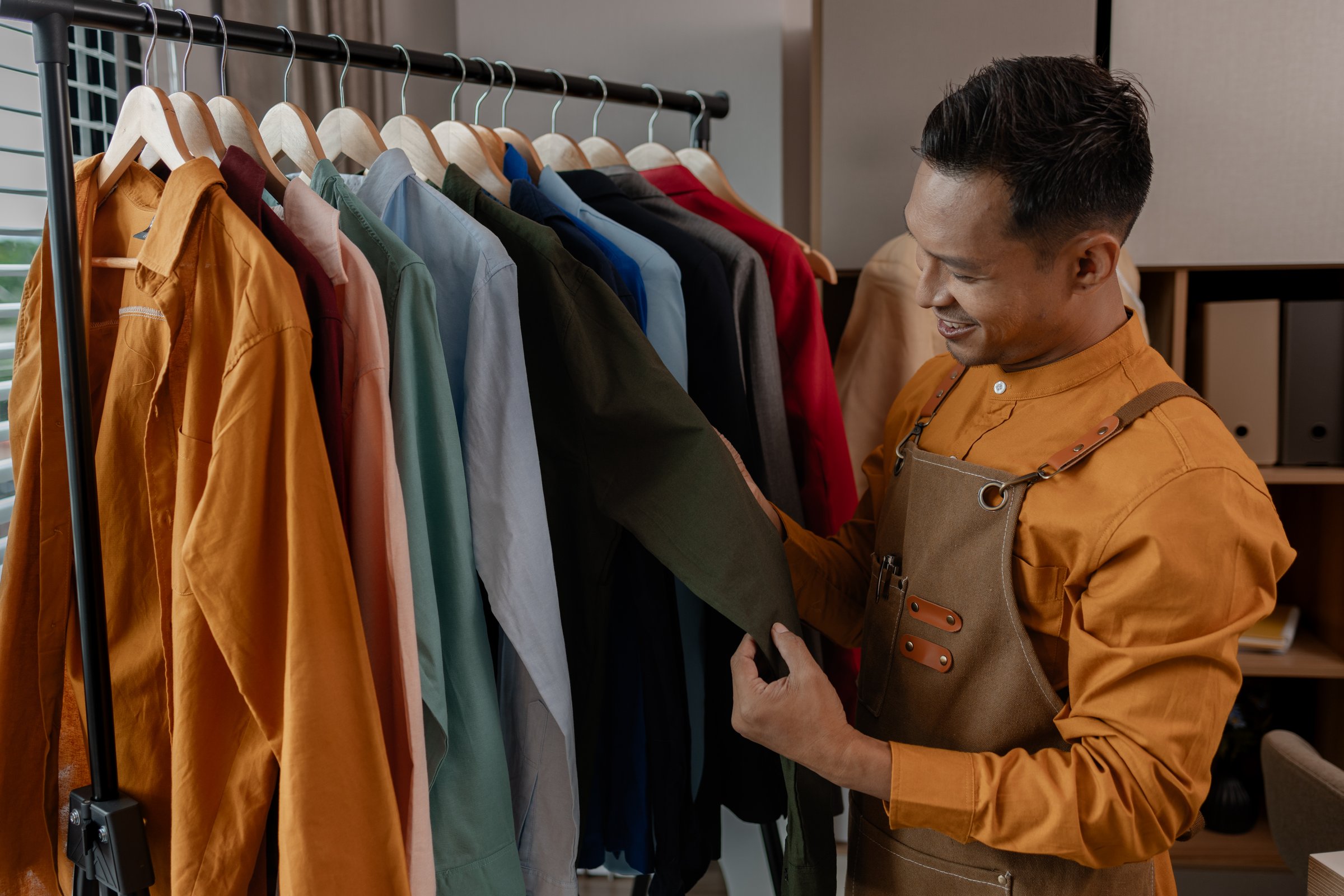 a designer is working in his studio, checking all clothes before sent to shop, talented designer is happy with his work, stylish. fabric, sewing, fashionable, entrepreneur