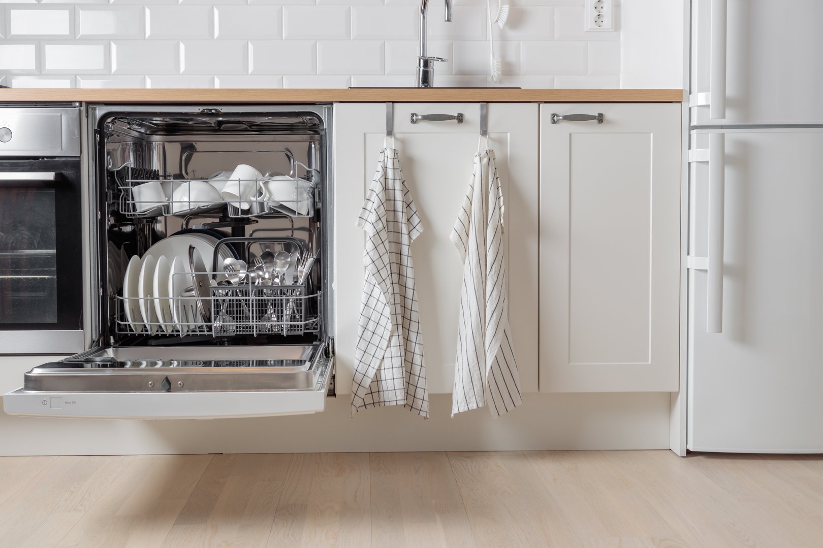 Built-in dishwasher full of clean dishes with its door open, white utensil. Modern technologies in the home kitchen with minimalistic cabinetry. Simplifying daily housework.