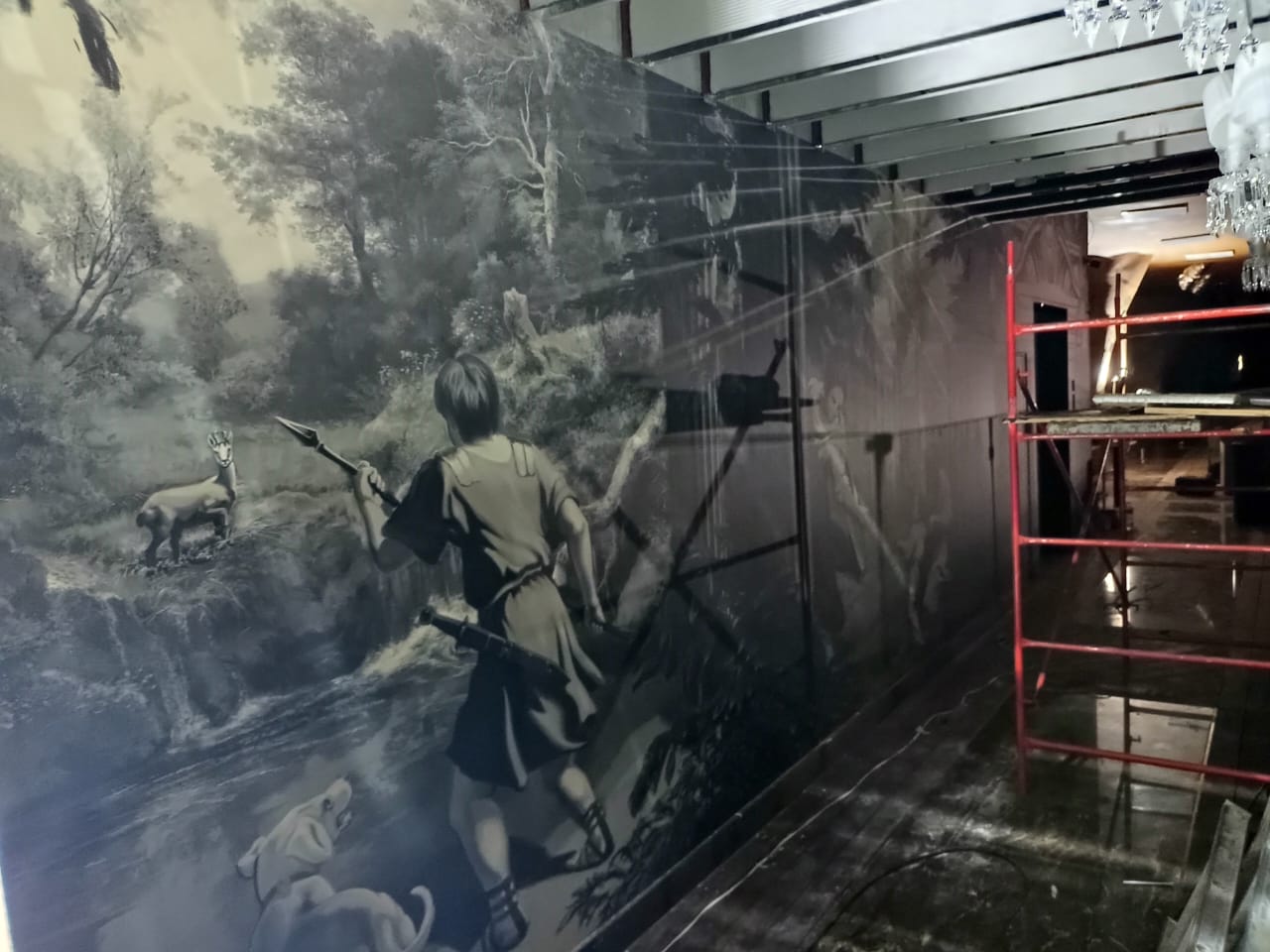 Mural depicting a hunter aiming at a stag, with a dog nearby. The scene is set in a forest, partially covered by scaffolding.