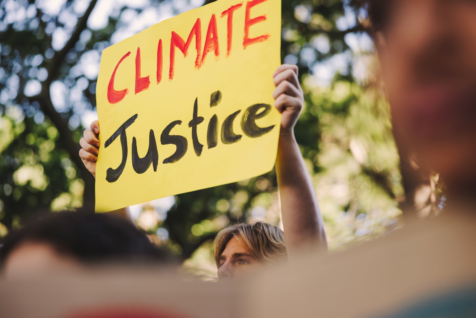 Movement for climate justice. Youth activist raising a poster while marching against climate change. Group of young people protesting against global warming and pollution.