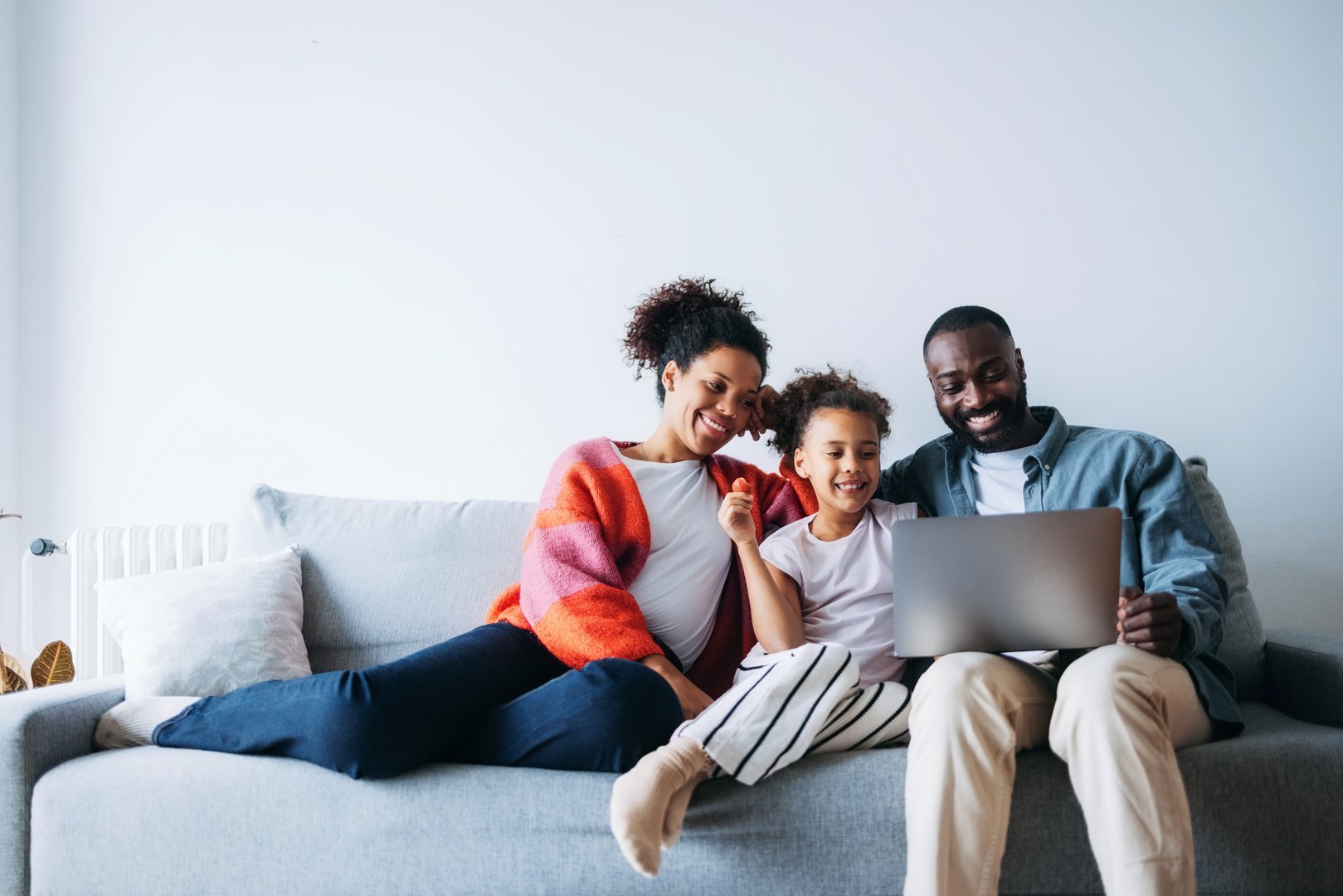 A joyful family sits together on a cozy sofa, sharing a moment as they look at a laptop, embodying happiness and togetherness in a comfortable and relaxed setting.
