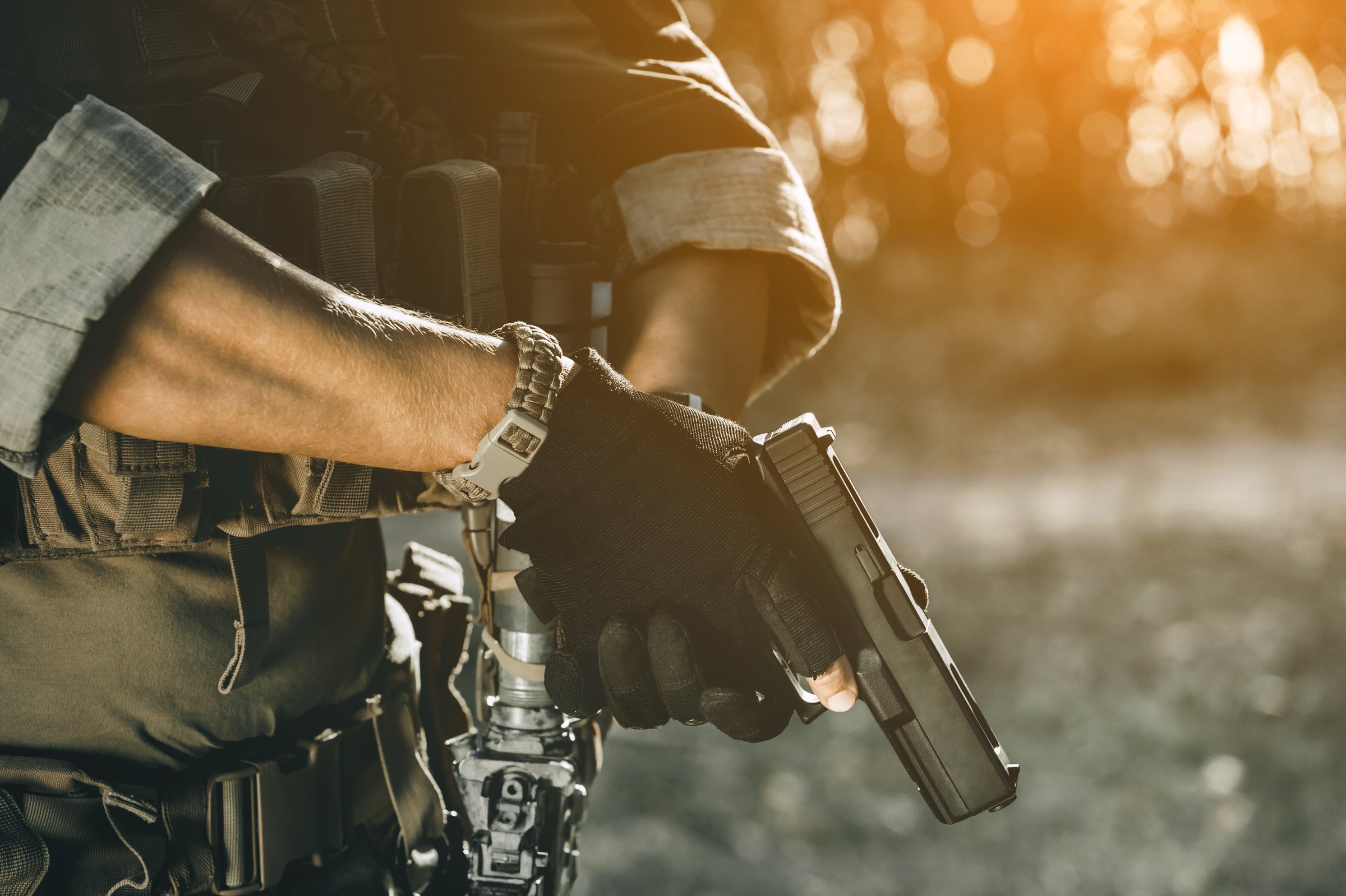the soldier in the performance of tasks in camouflage and protective gloves holding a pistol. War Zone.