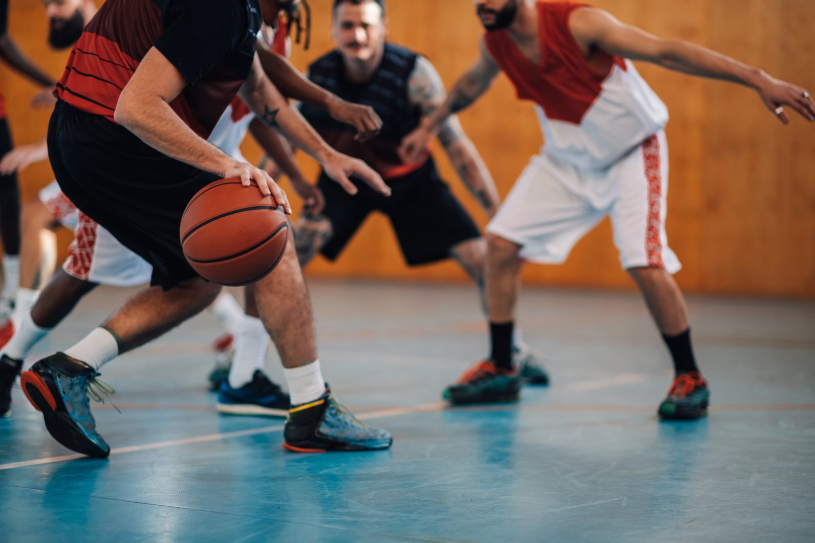 Unrecognizable diverse professional players playing basketball at the gymnasium or a sports hall while having a practice or a match. Focus on a basketball ball while man is dribbling it. Copy space.