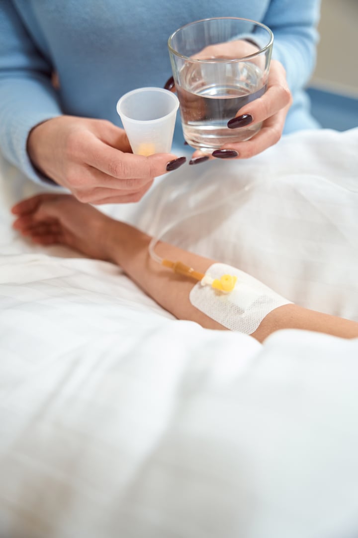 Adult woman gives pills and glass of water to a sick child, a fixing patch is on the child's hand