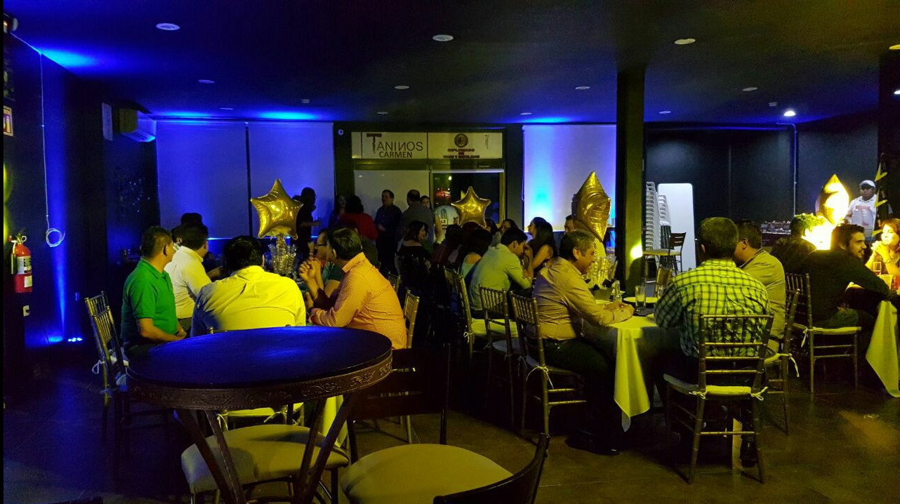 People seated at tables in a dimly lit room with blue lighting and gold star-shaped balloons, participating in a social event.