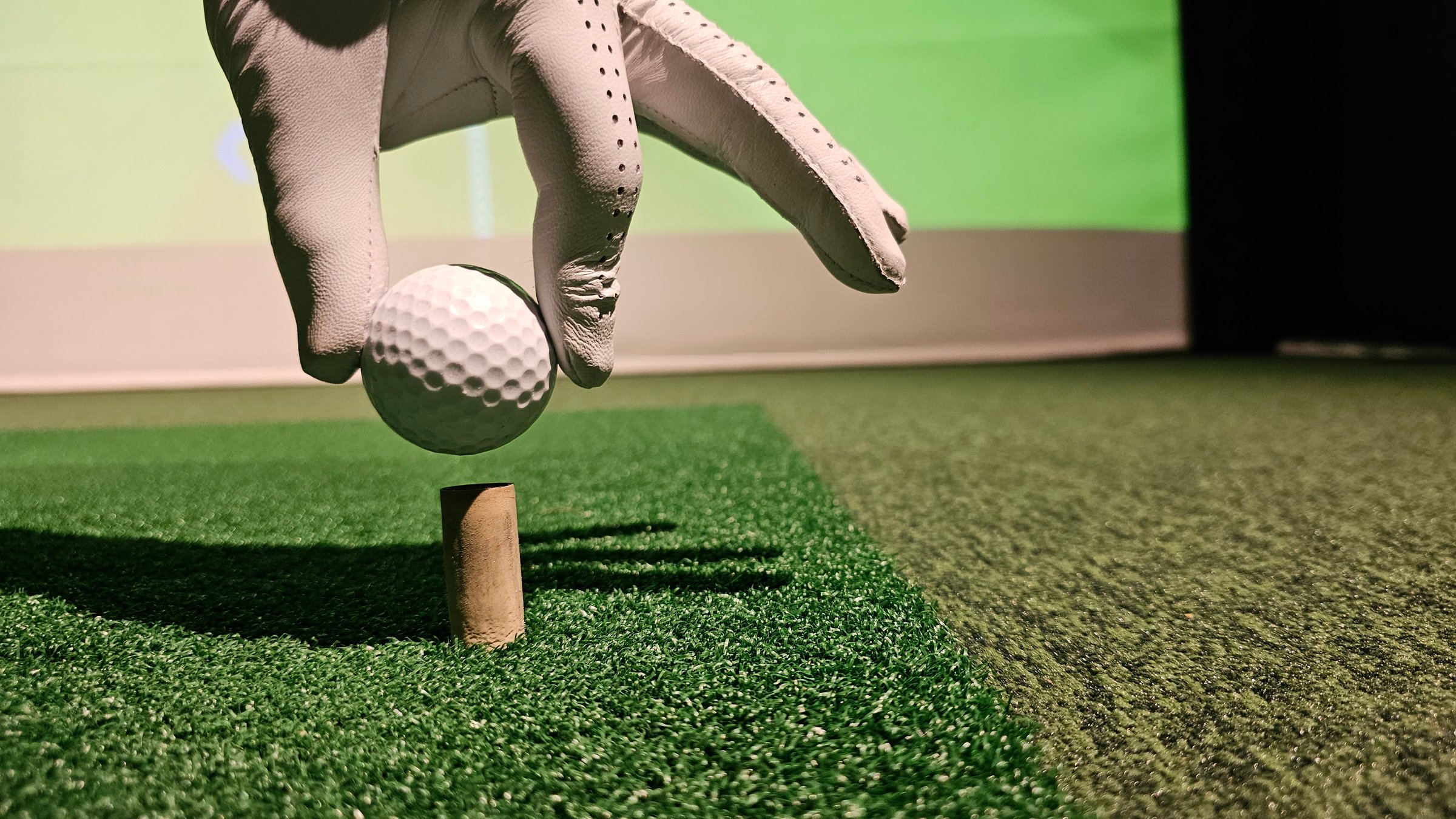 Golfer in glove holds golf ball and club indoors. Playing golf on a simulator