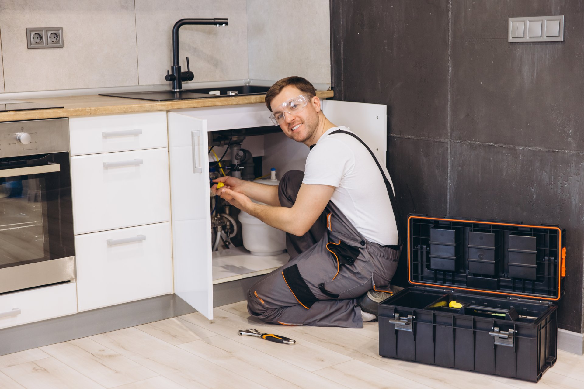 Professional plumber working on installing or repairing water filter system under sink in modern kitchen