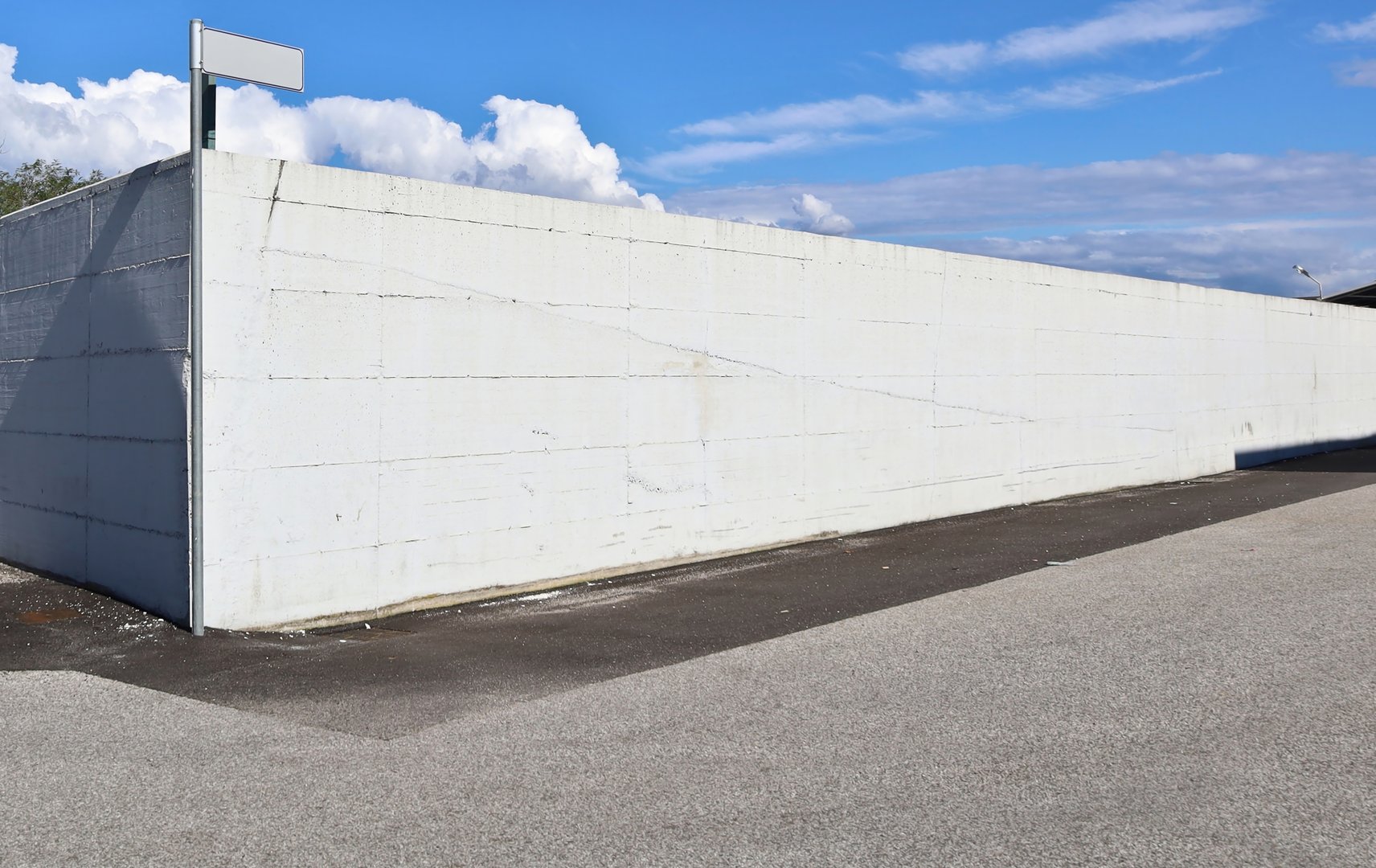 Large white concrete surrounding wall at the corner of a street. Blue sky with clouds above. Background for copy space.