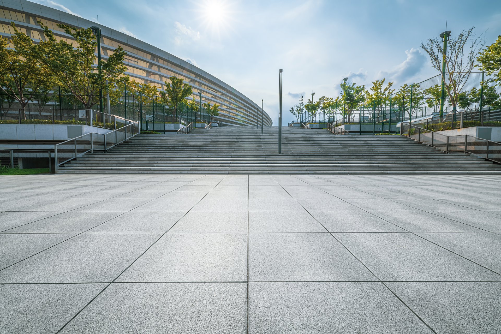 Broad stone plaza with imposing staircase leads up to a contemporary public edifice under a vivid blue sky.