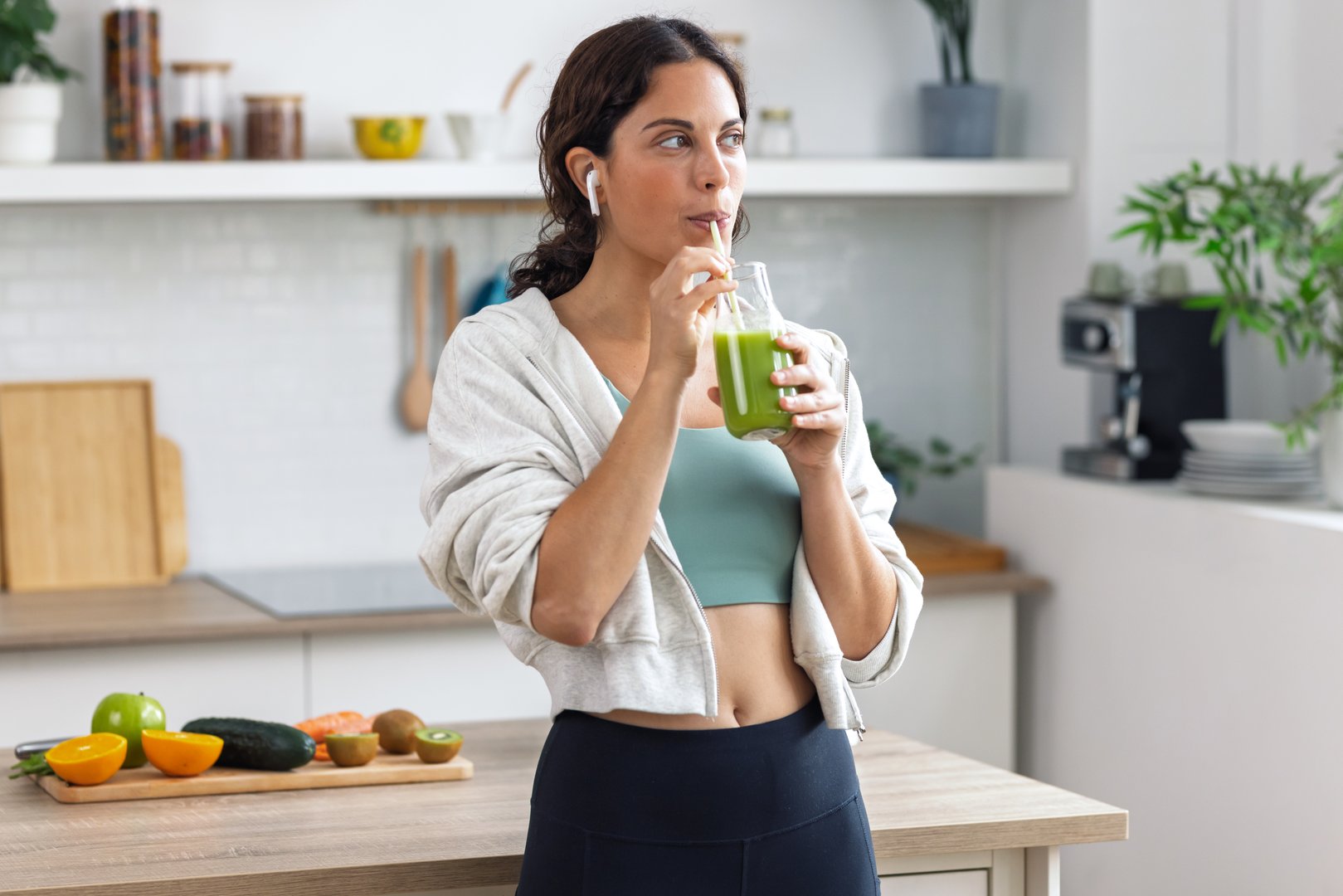 Shot of kind sporty woman drinking a healthy green smoothie standing in the kitchen at home - Hydration and Performance Nutrition at SugarFree.Space