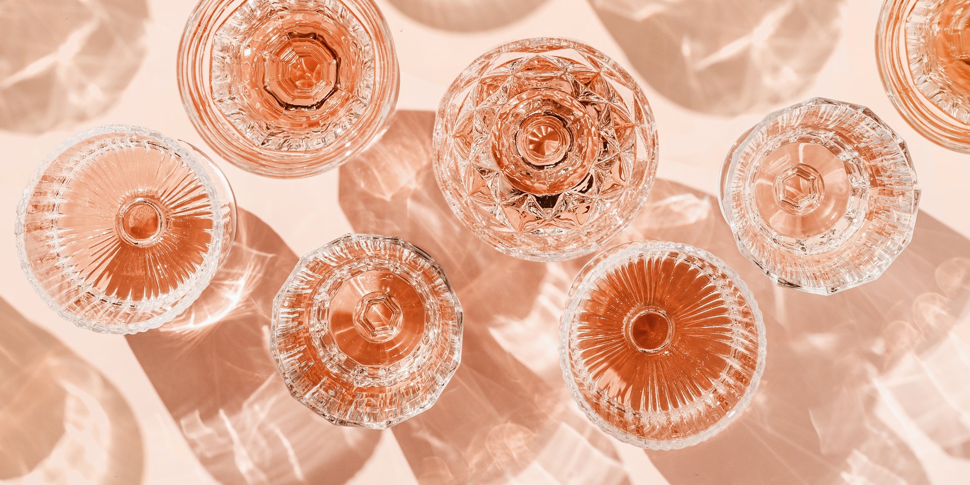 Stylish banner of rose wine crystal glasses casting shadows on pastel peach background. Minimal Top view sparkling alcohol drinking, champagne drinks at sunlight, wine aesthetic party concept