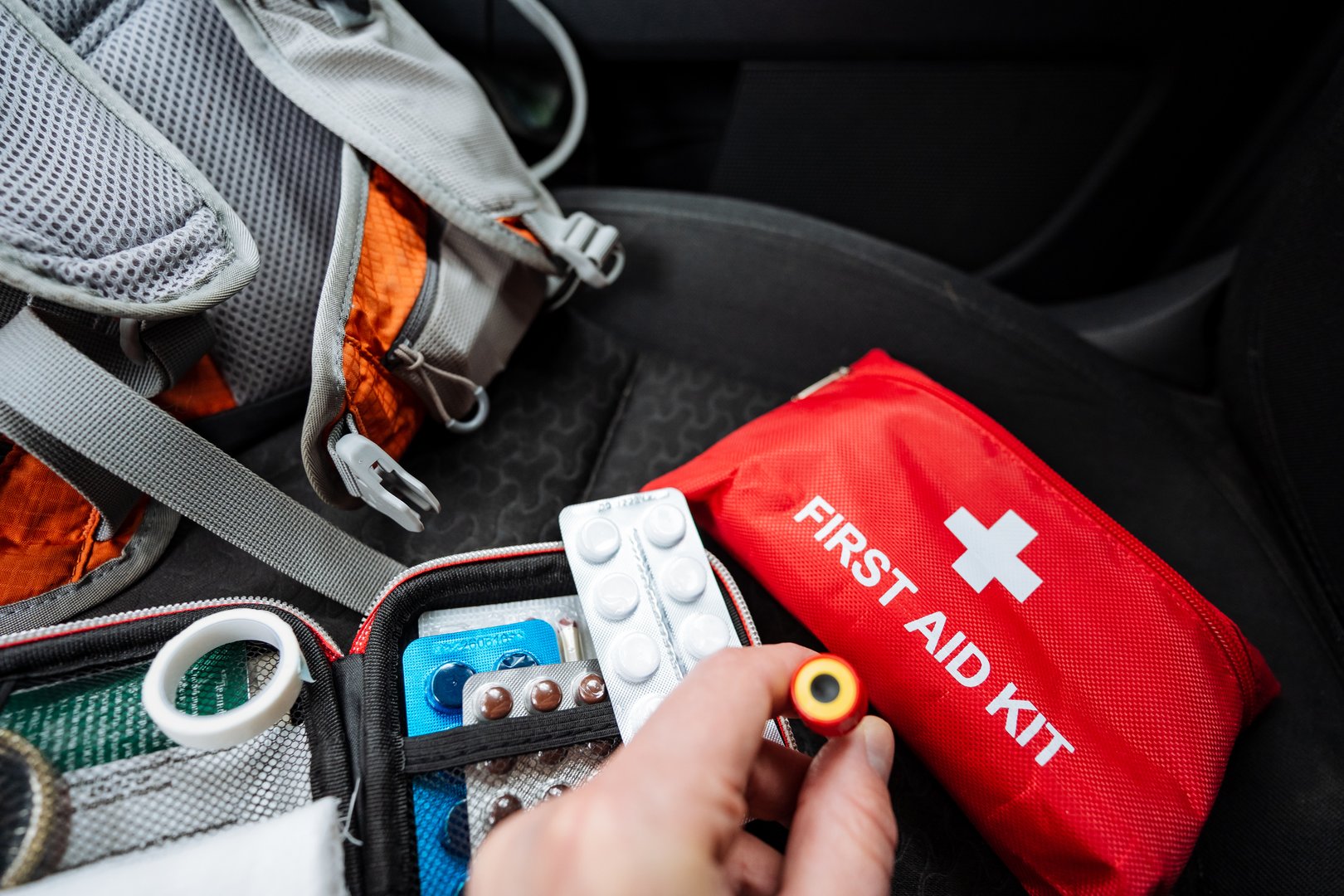 In a critical situation, a person is quickly opening a first aid kit in a car to address an urgent injury, highlighting the need for immediate and effective care to ensure everyones safety