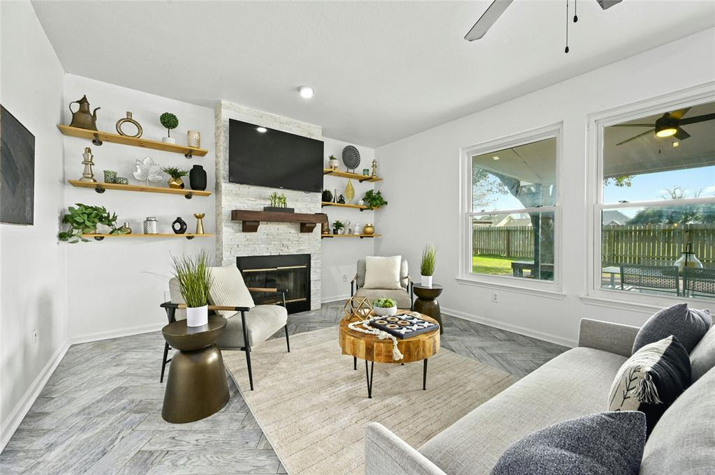 Modern living room with fireplace, wall-mounted TV, shelves with decor, contemporary furniture, and large windows.