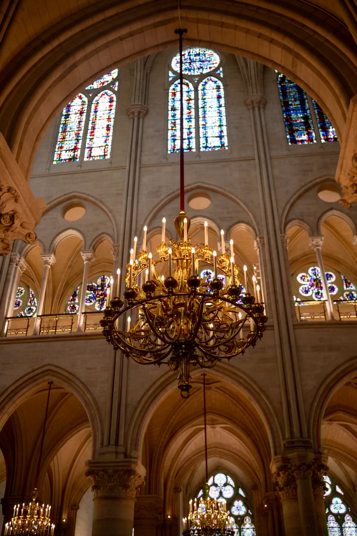 Paris, France-April 16, 2025: Ornate golden chandelier hangs under gothic arches with colorful stained glass windows inside Notre-Dame Cathedral.
