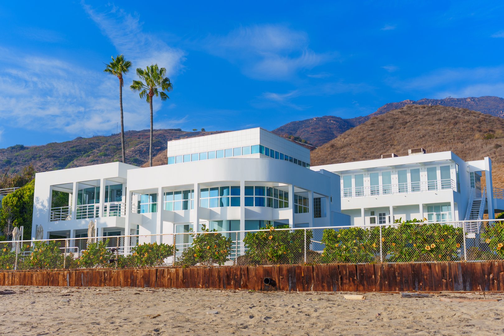 Malibu, California - December 21, 2024: Breathtaking view of a contemporary beachfront house surrounded by palm trees and hills, ideal for luxury living and coastal escapes.