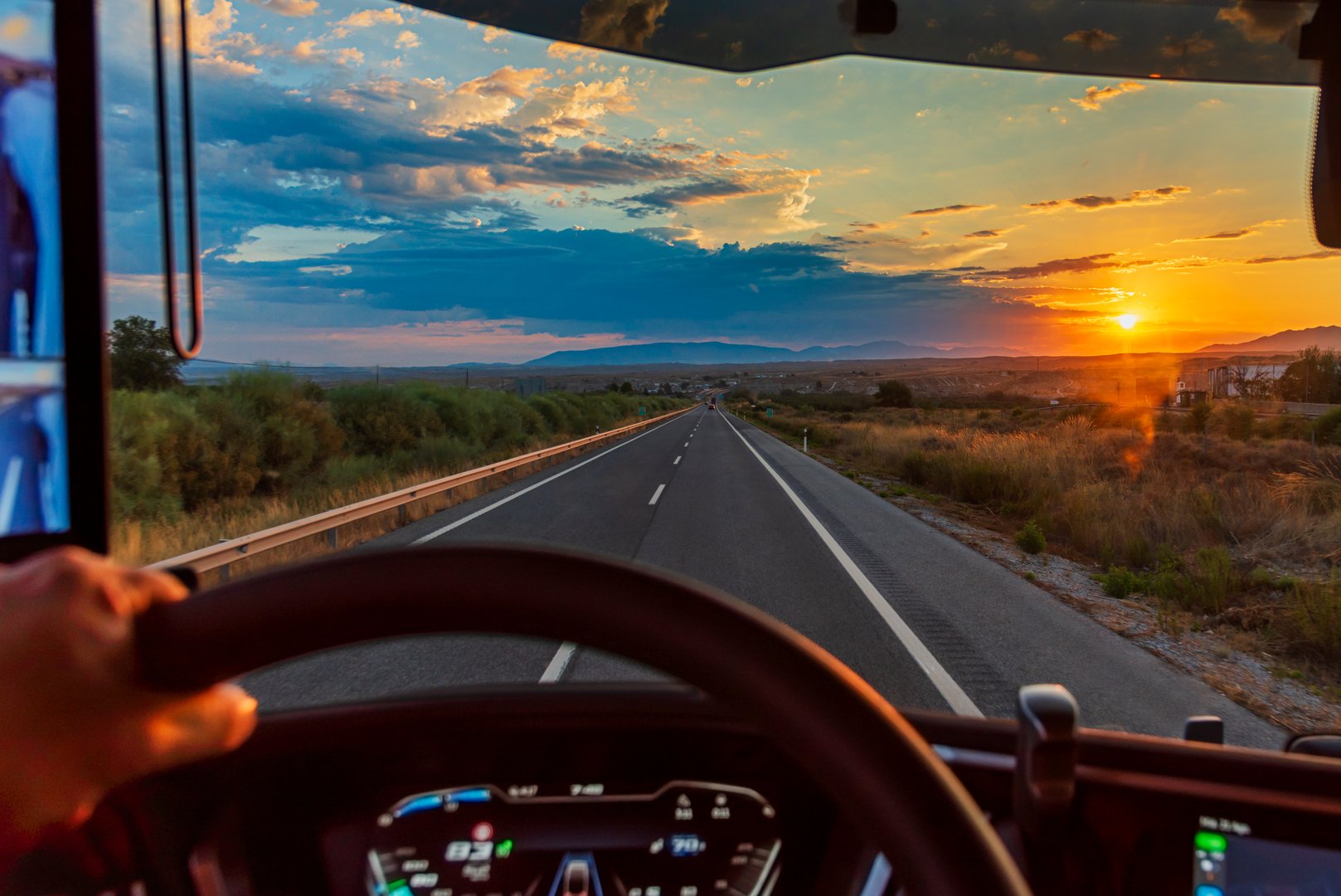 View from the driver's seat of a truck on a highway at dawn with the sun on the horizon.