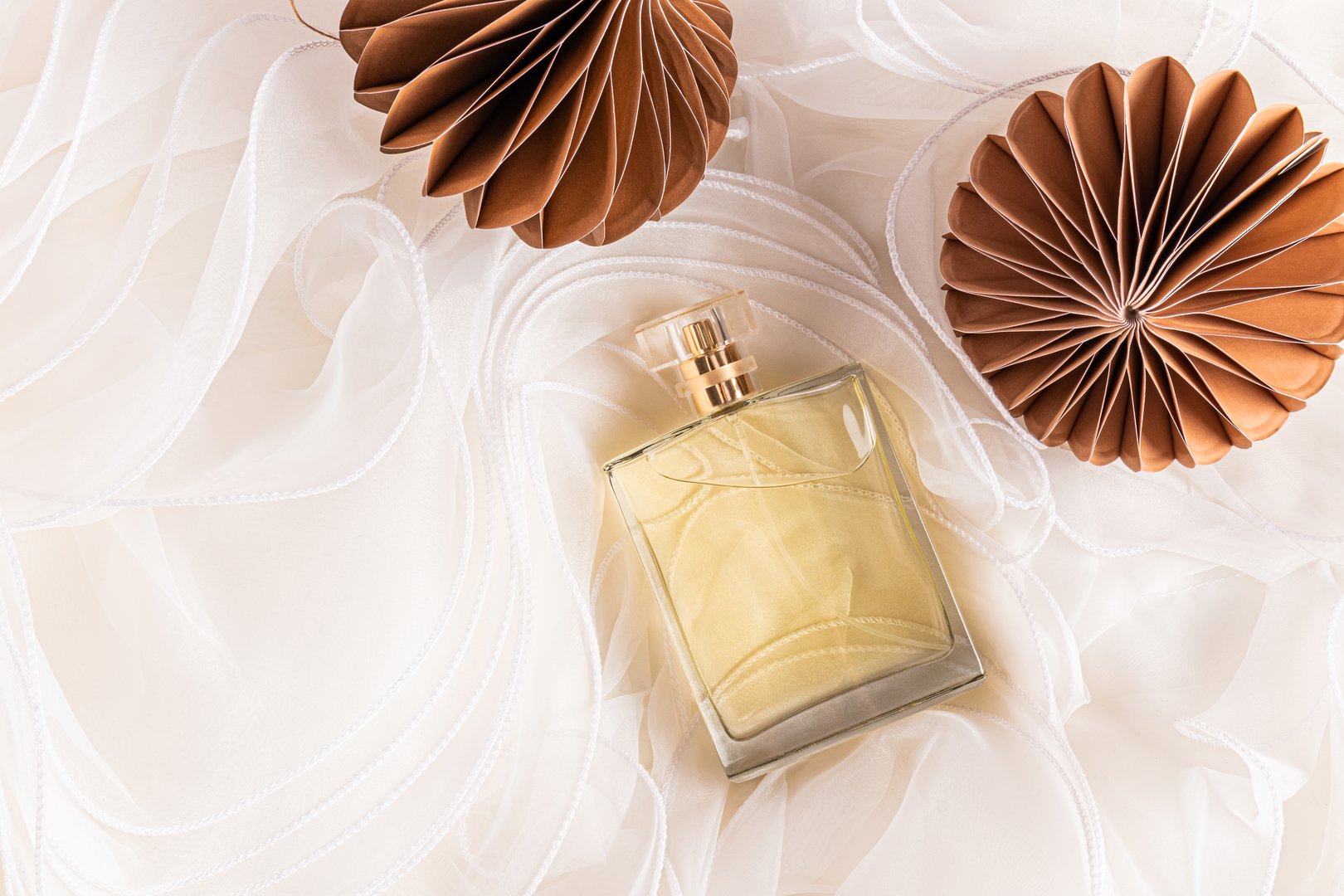 A chic unbranded bottle of perfume on a brown honeycomb paper toy. Beige chiffon fabric background. New Year's presentation of the fragrance