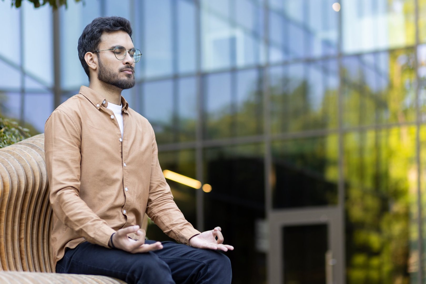 Young man practicing meditation outdoors while seated, focusing on relaxation and mindfulness. Professional taking office break to find peace clarity in urban setting, emphasizing stress reduction .