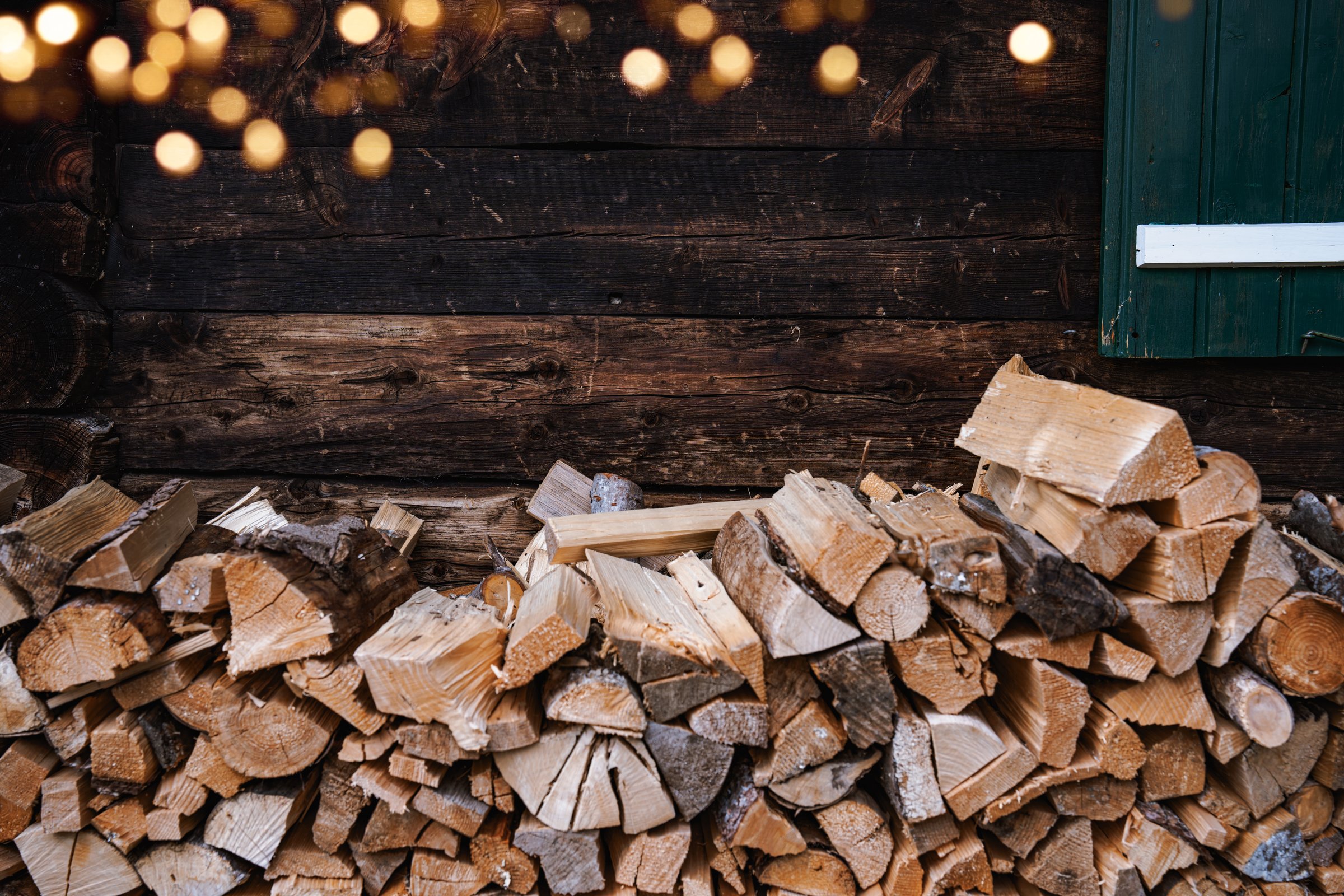 Stack of firewood along an outside wall of a hause with golden bokeh. Rustic background for wintertime.