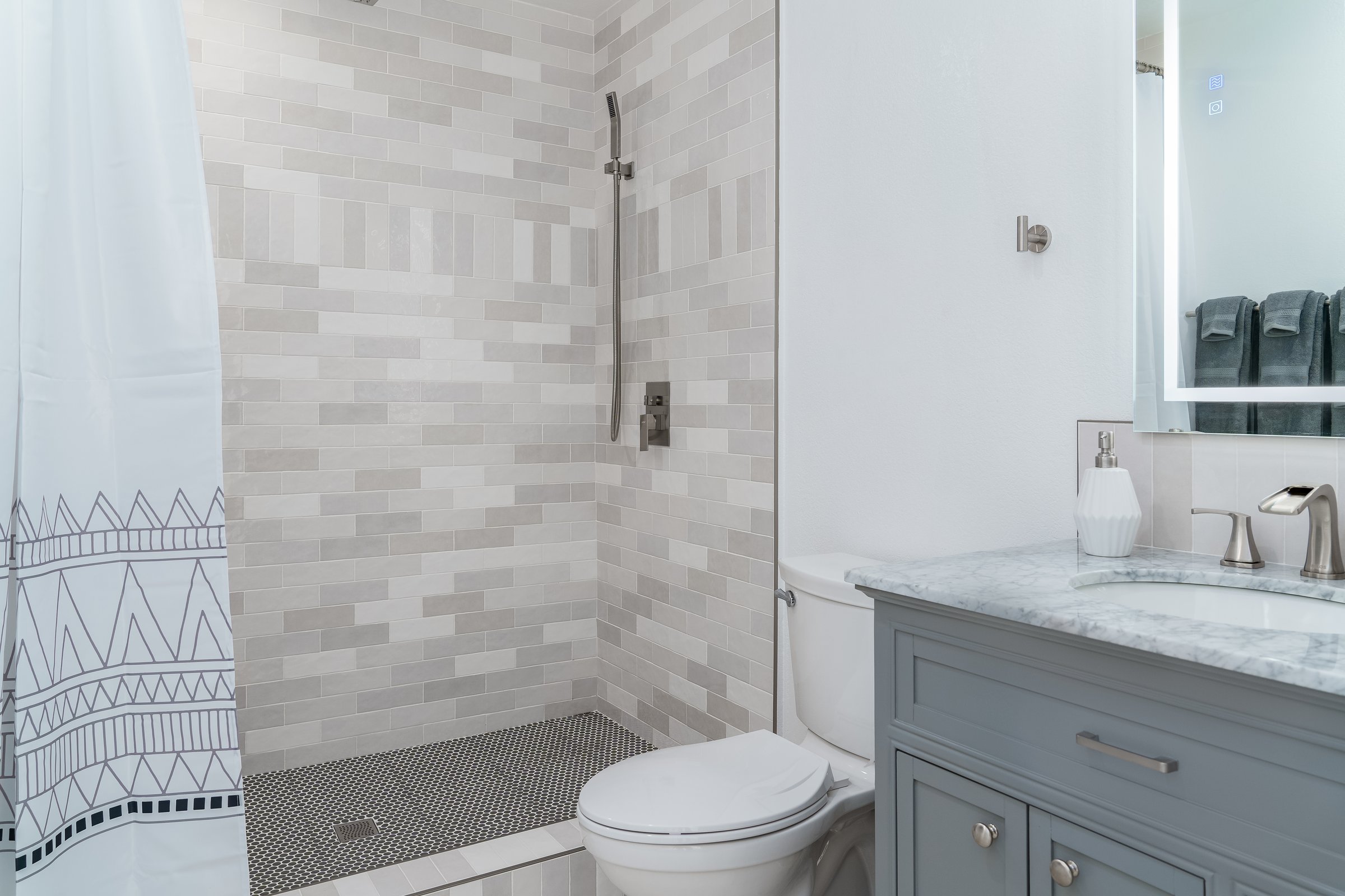 modern bathroom in white with gray tile shower, painted wood cabinet, and marble sink