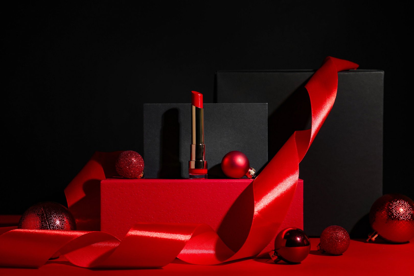 Christmas present. Red lipstick, boxes and festive decor against black background