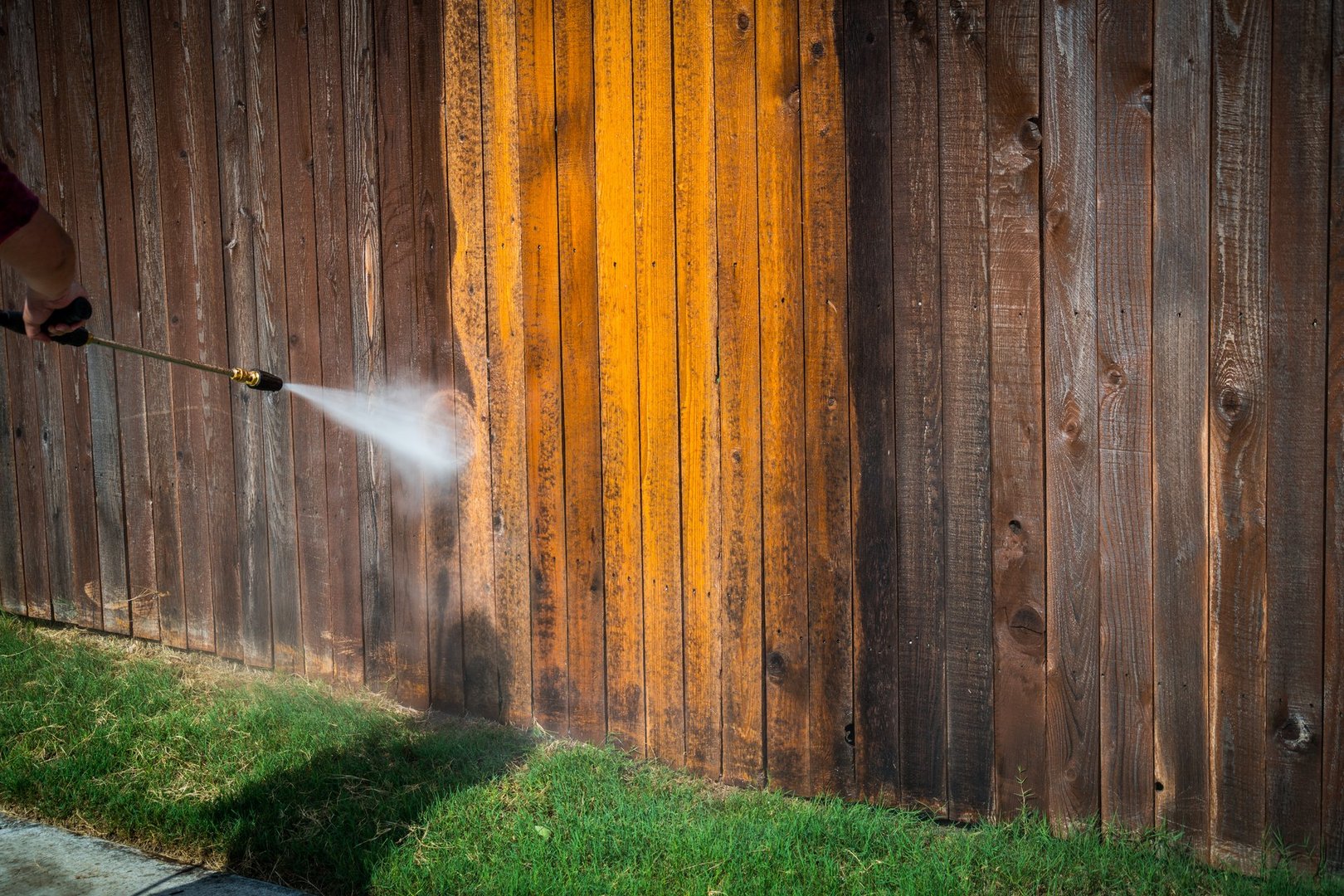 Spraying the top of a Wooden fence spraying a high Pressure washing a dirty grimy old wooden fence and turning it from dirty to clean in a matter of second with spray blast from pressure washer with grass and sidewalk