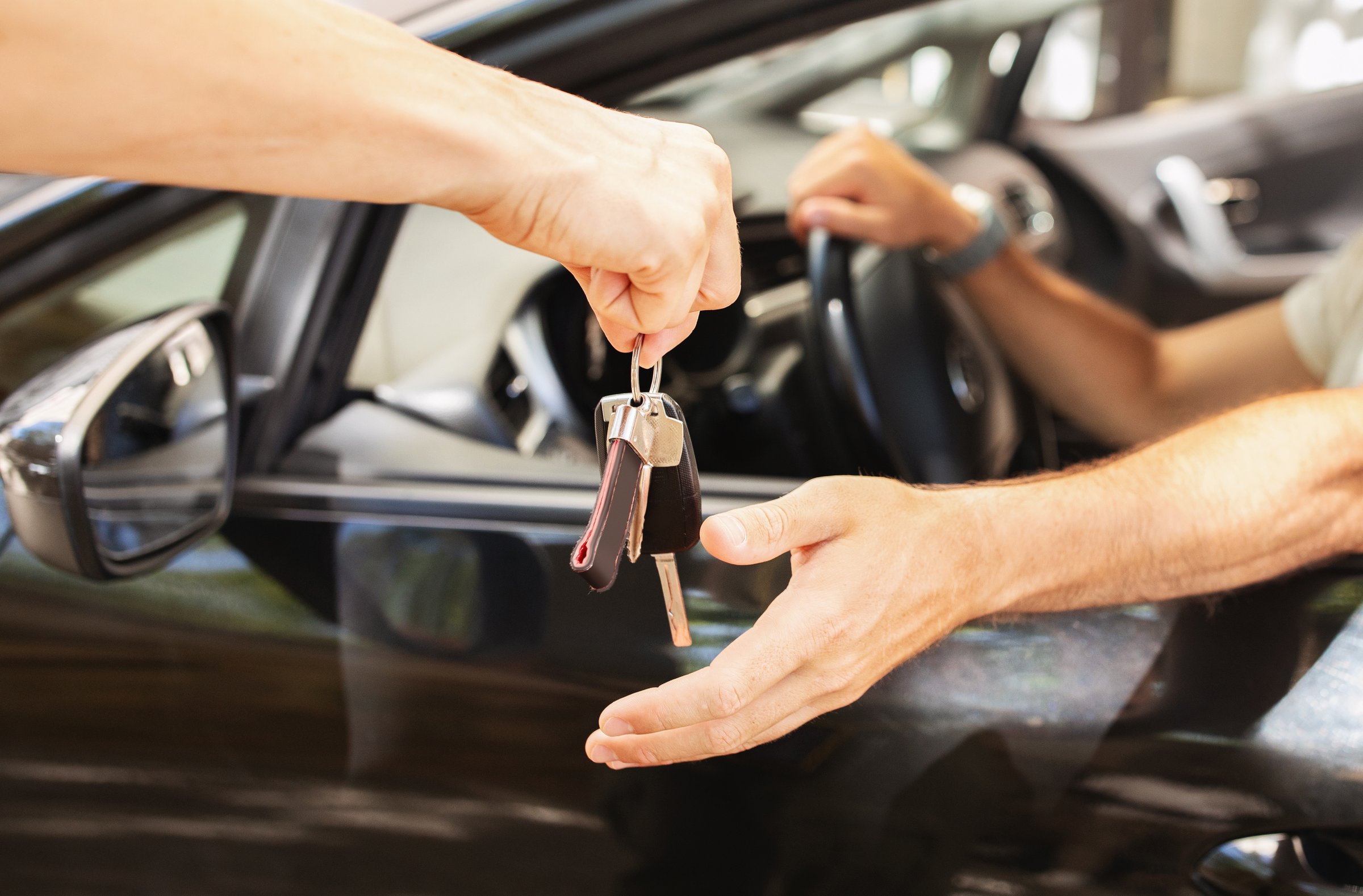 Hands of valet parking worker giving key to driver man sitting inside car. Unrecognizable man buyer taking key from brand new automobile at autosalon showroom. Car buying, renting