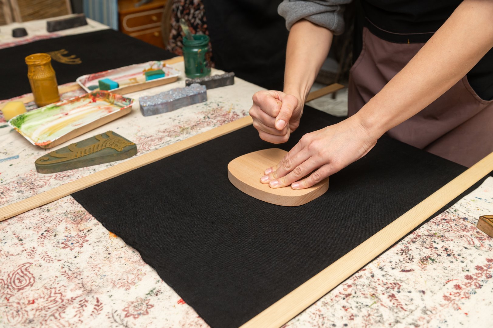 Female artisan printing on fabric with wooden block in craft studio.