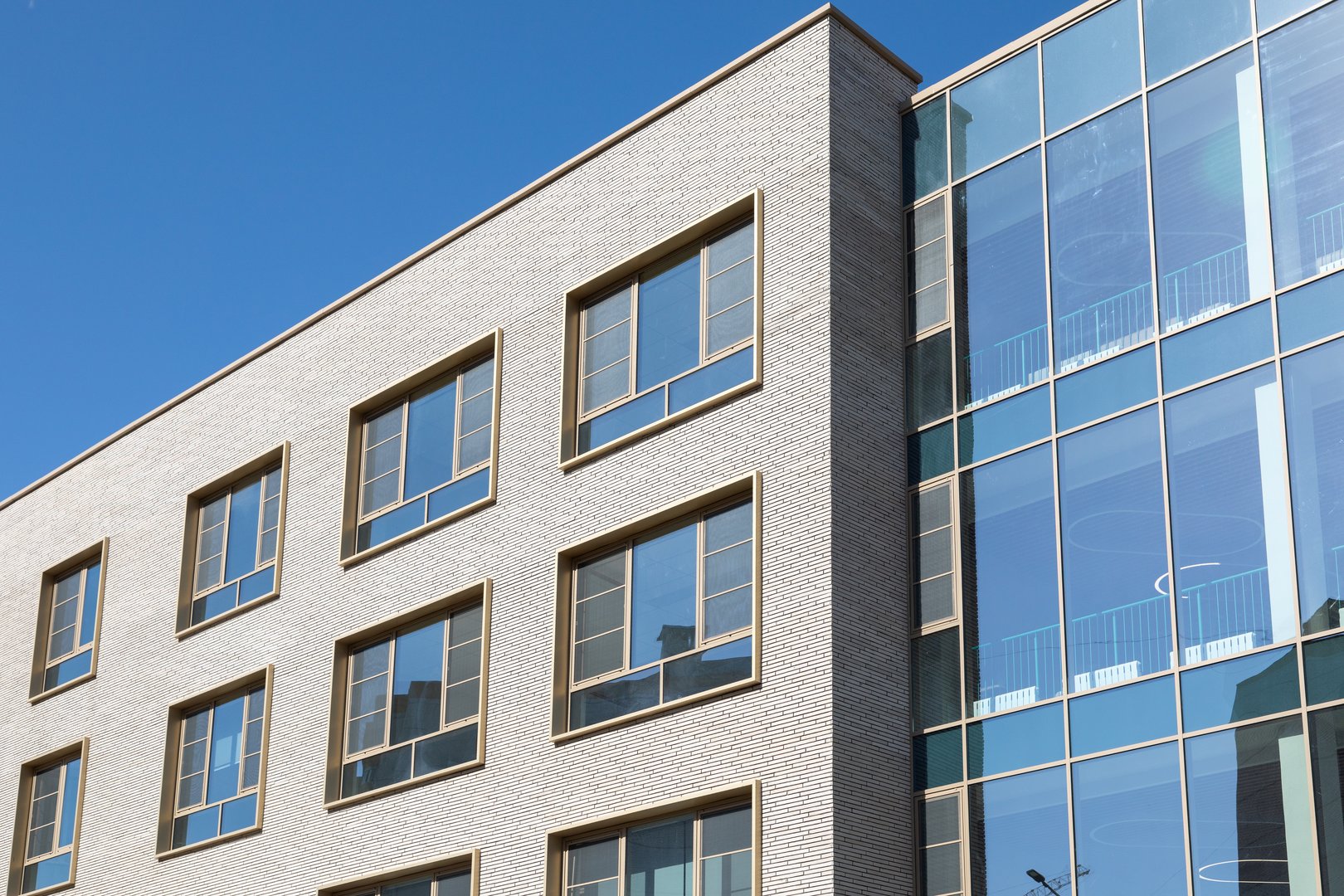 Modern building facade with brick and glass panels under blue sky. Clean architectural lines for commercial or residential projects. Brick exterior with large windows and reflective glass section