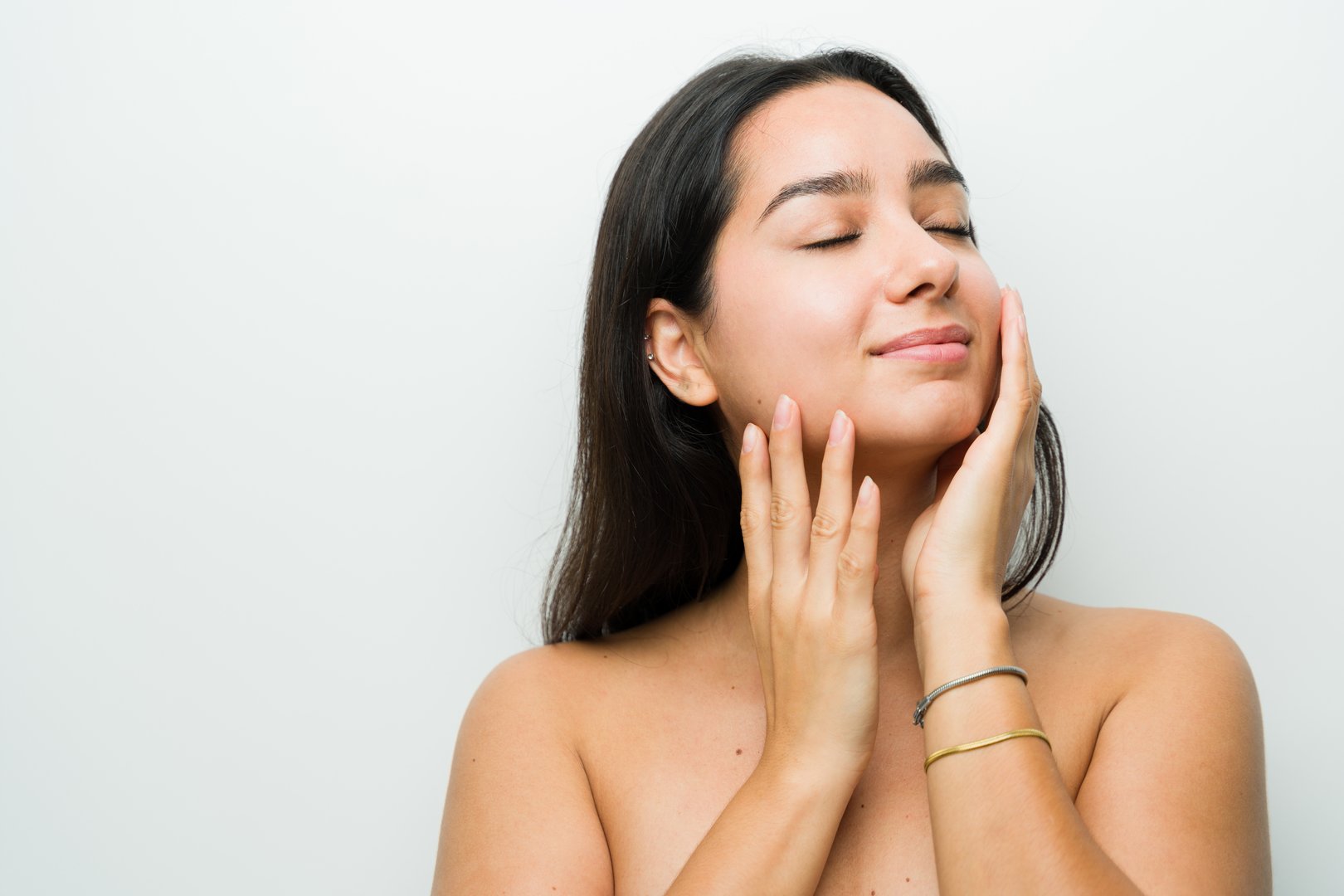 Elegant hispanic woman indulges in a soothing skincare treatment in a bright studio setting, radiating natural beauty and self-care satisfaction